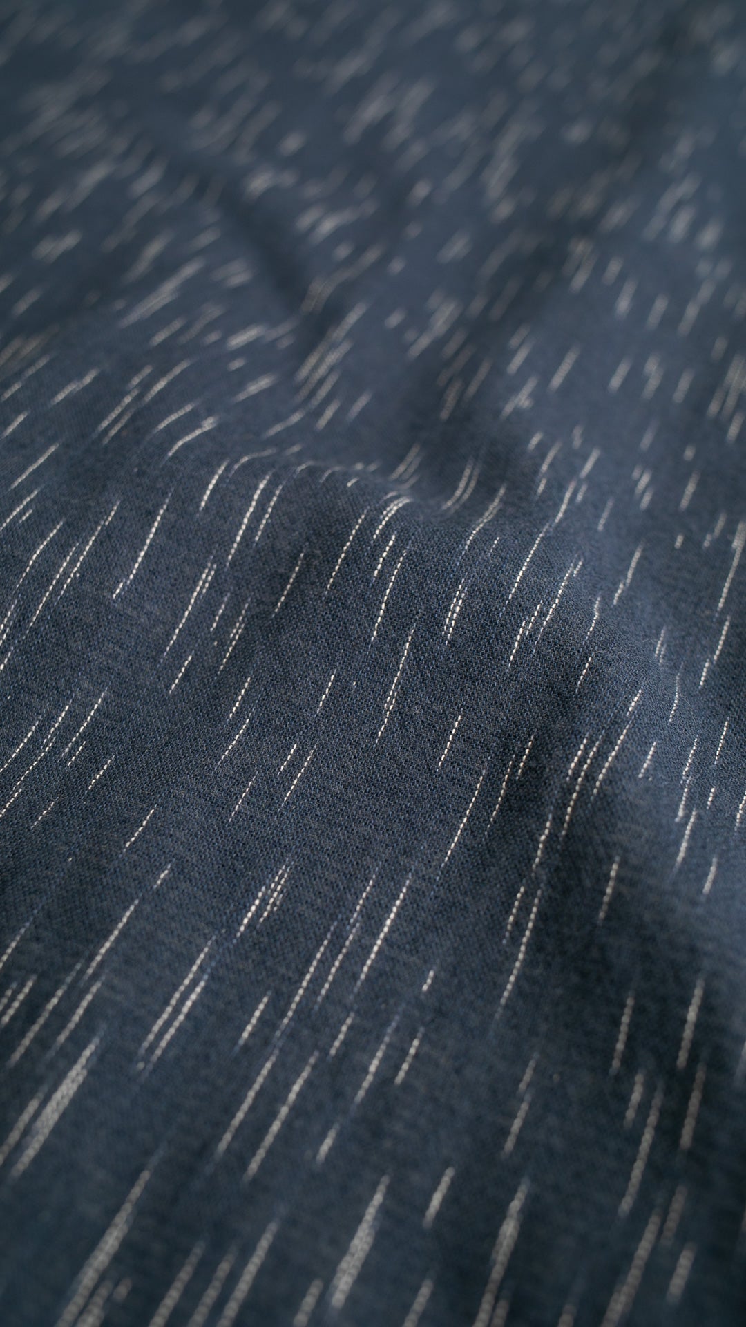 Close-up of dark blue fabric with thin, white, irregular vertical lines resembling a rain pattern. The material appears soft with slight wrinkles and a textured surface.