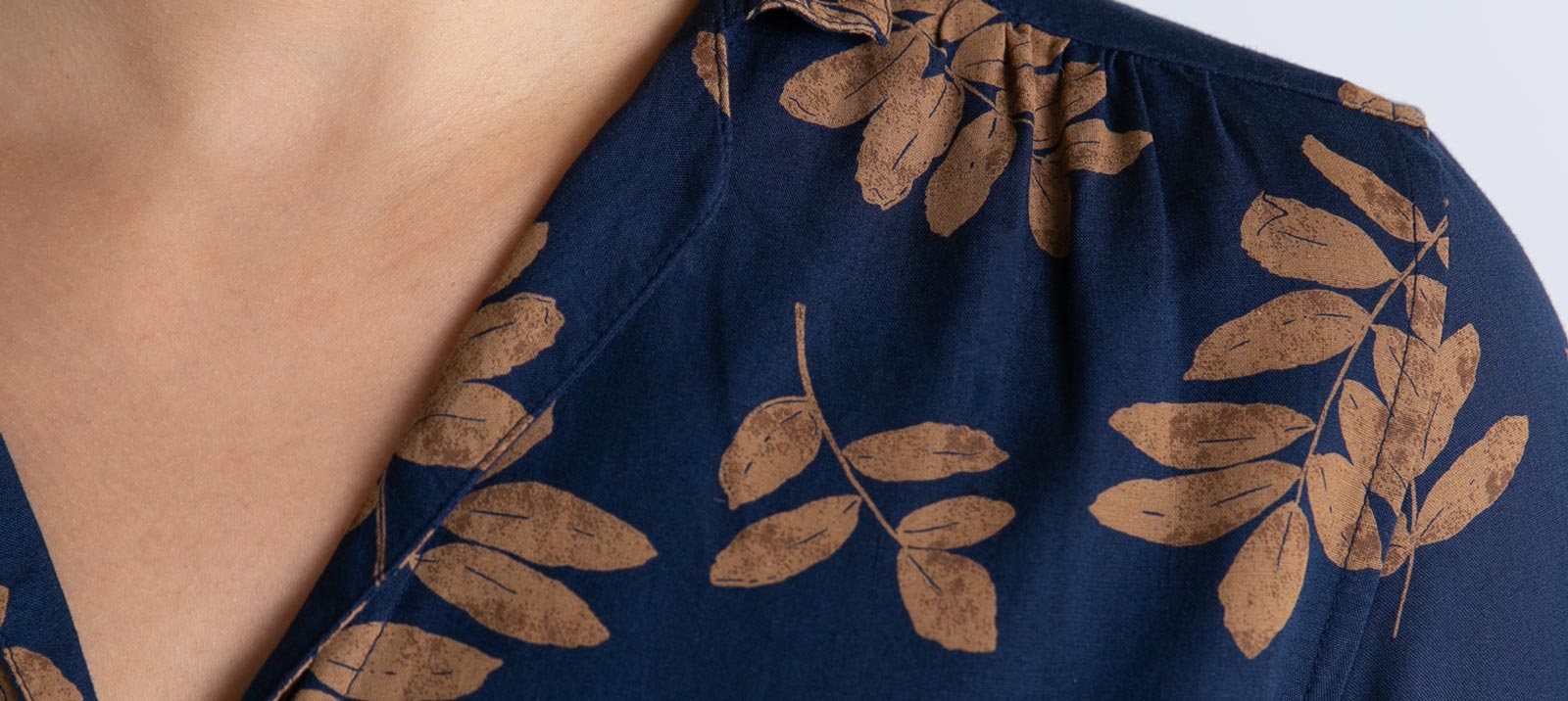 Close-up of a person wearing a dark blue shirt with a brown leaf pattern. The shirt has a collar, and only the lower part of the neck and upper chest are visible.