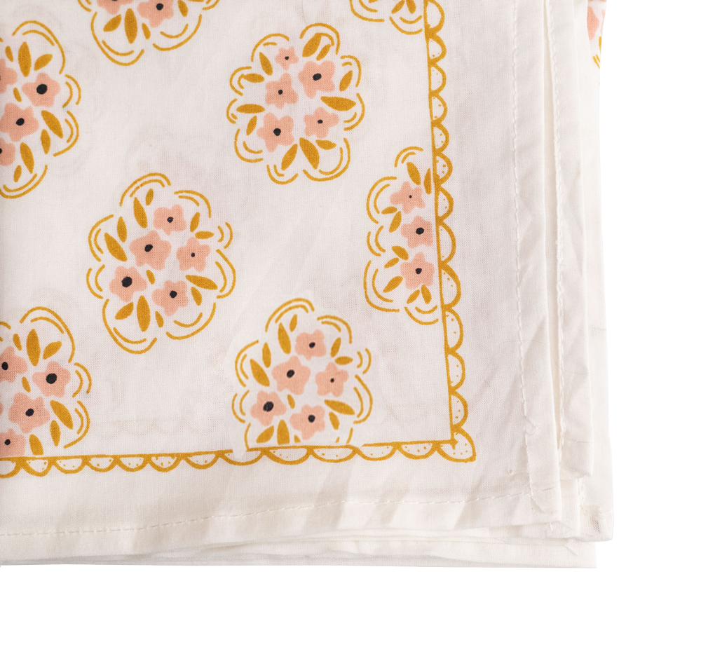 The Handker Bandanas - No. 042 Pearl Bandana by Handker Bandanas is a white cotton napkin with a yellow scalloped border and delicate pink and yellow floral clusters near the edges.