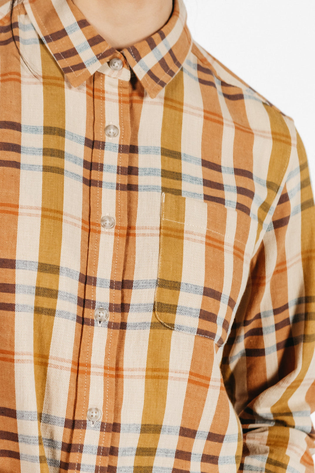 A person wears the Ash Slim Shirt / Heceta Plaid by Bridge & Burn, a beige, brown, and yellow slim fit button-up with a small chest pocket. The image shows the upper torso and part of the collar.