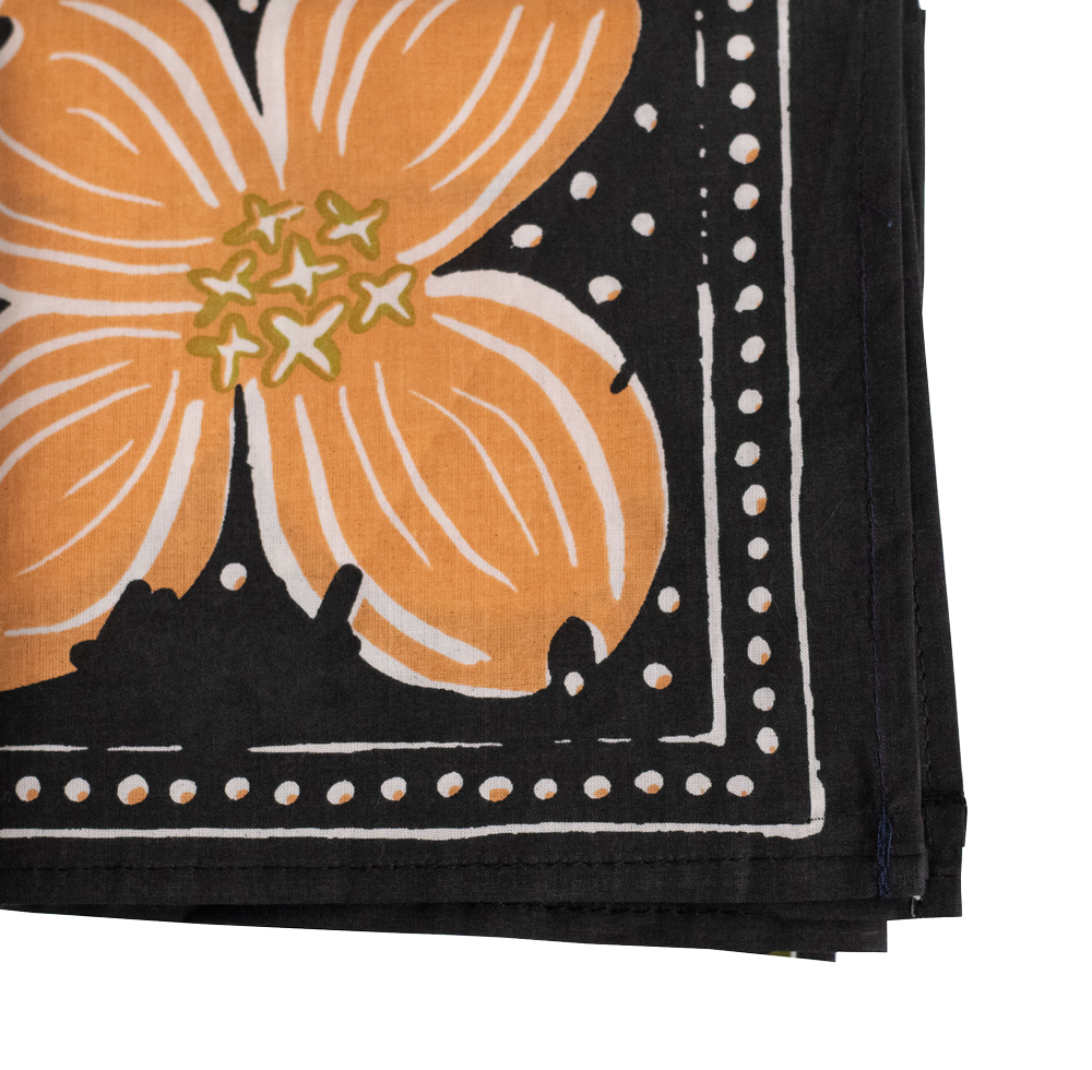 The Handker Bandanas - No. 046 Amy Bandana by Handker Bandanas is a folded black cotton bandana with a bold orange dogwood flower and white dotted border; only part of the flower and border are seen.