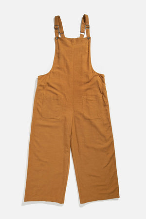 The Edie Overall in Ochre by Bridge & Burn features a loose, wide-leg fit, adjustable shoulder straps, and two large front pockets in a linen-cotton blend, shown laid flat on a white background.