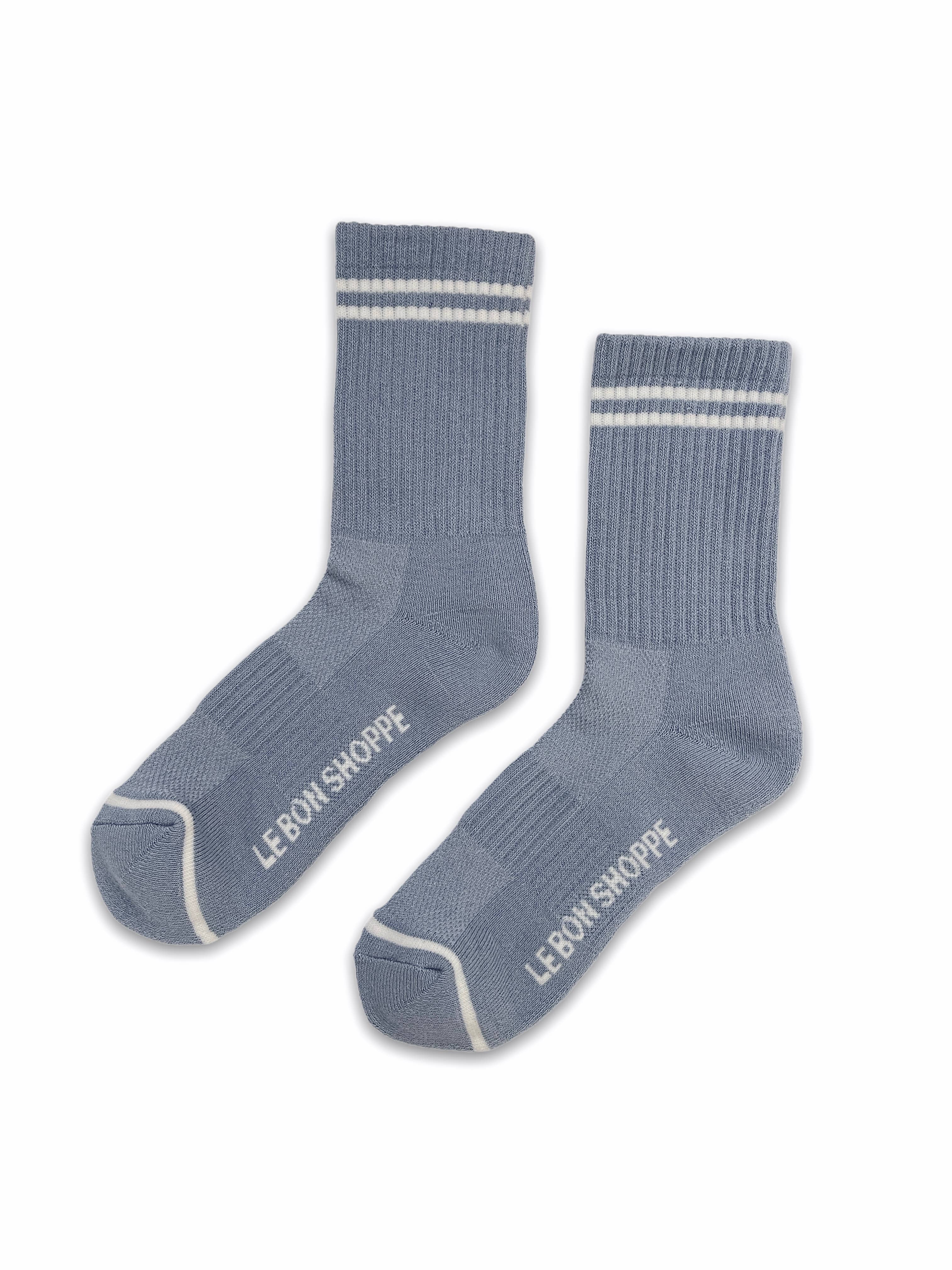 A pair of Le Bon Shoppe Boyfriend Socks in Blue Grey, featuring two white stripes at the top, sporty white accents on the toes, and "Le Bon Shoppe" written in white on the soles.