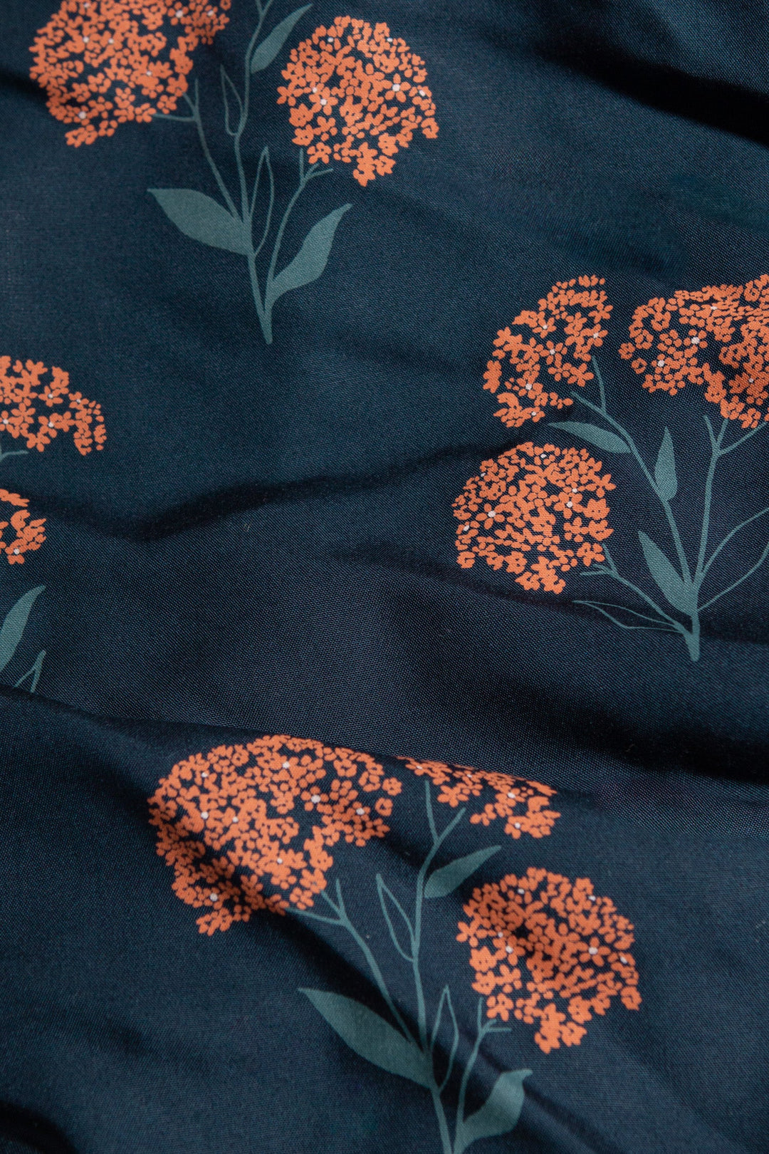 The Sofia Shirt Dress in Wildflower by Bridge & Burn features dark blue fabric with orange floral clusters and green stems in a repeating design. Its slightly wrinkled texture adds charm to this sustainable summer button-front dress.