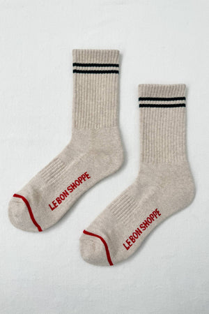 Le Bon Shoppe Boyfriend Socks in Oatmeal feature black double stripes near the top, “LE BON SHOPPE” in red on the soles, a ribbed texture, and sporty red accents at the toe and heel.