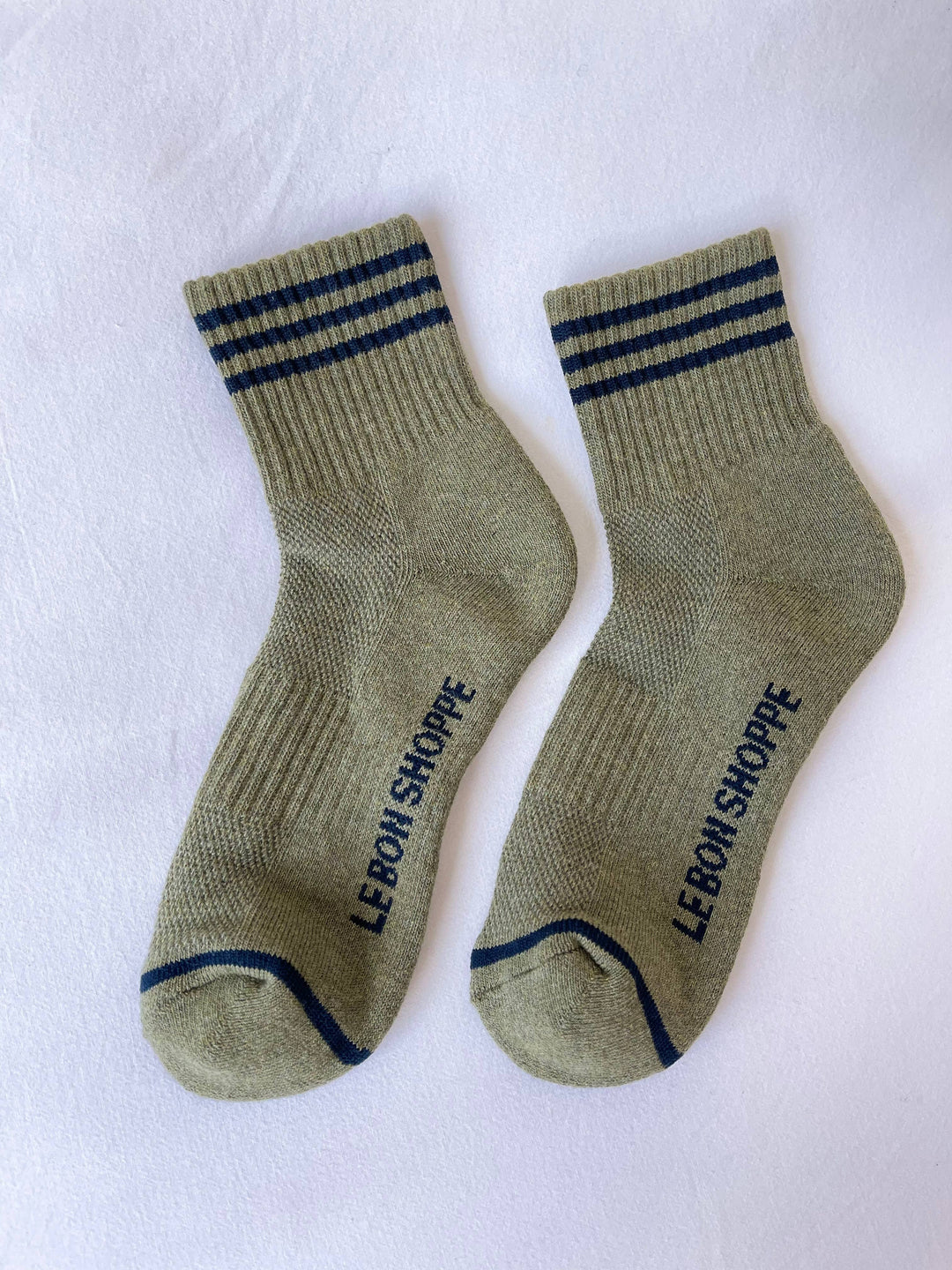 Le Bon Shoppe - Girlfriend Socks in Sage: Light olive green crew socks with dark blue top stripes and “LE BON SHOPPE” printed in blue on the soles, shown on a white background.