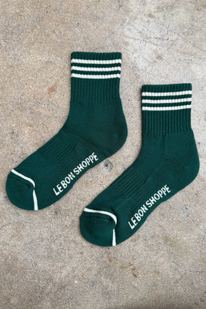 The Le Bon Shoppe - Girlfriend Socks in Hunter Green feature ribbed crew style, white top stripes, and “LE BON SHOPPE” on the soles—perfect women’s socks for daily comfort. Displayed on a textured concrete surface.