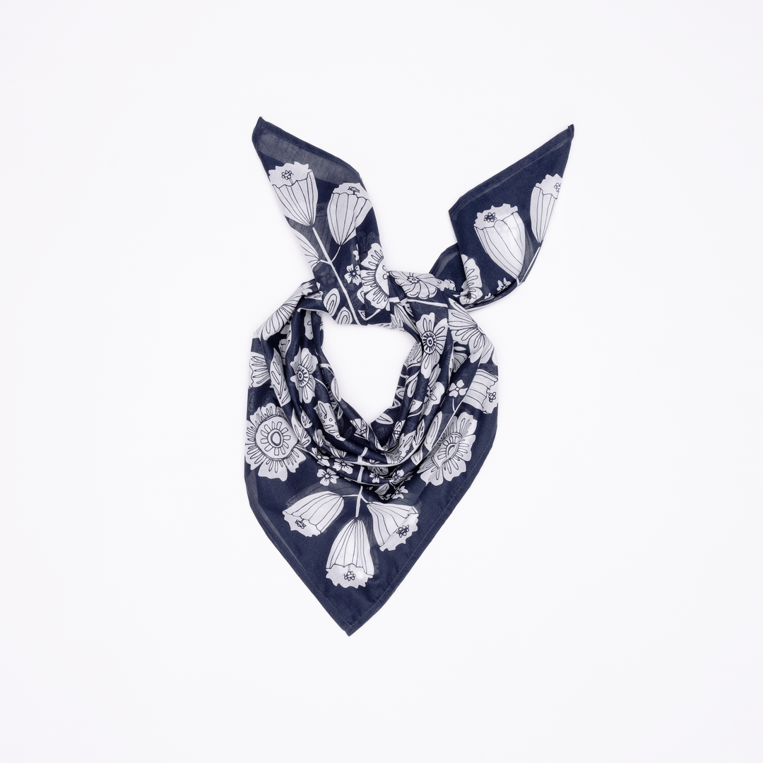 The Handker Bandanas 34" Wild Rag Fiona Bandana in dark blue cotton lawn with white florals is hand screen-printed, folded, and loosely knotted for display on a white background.