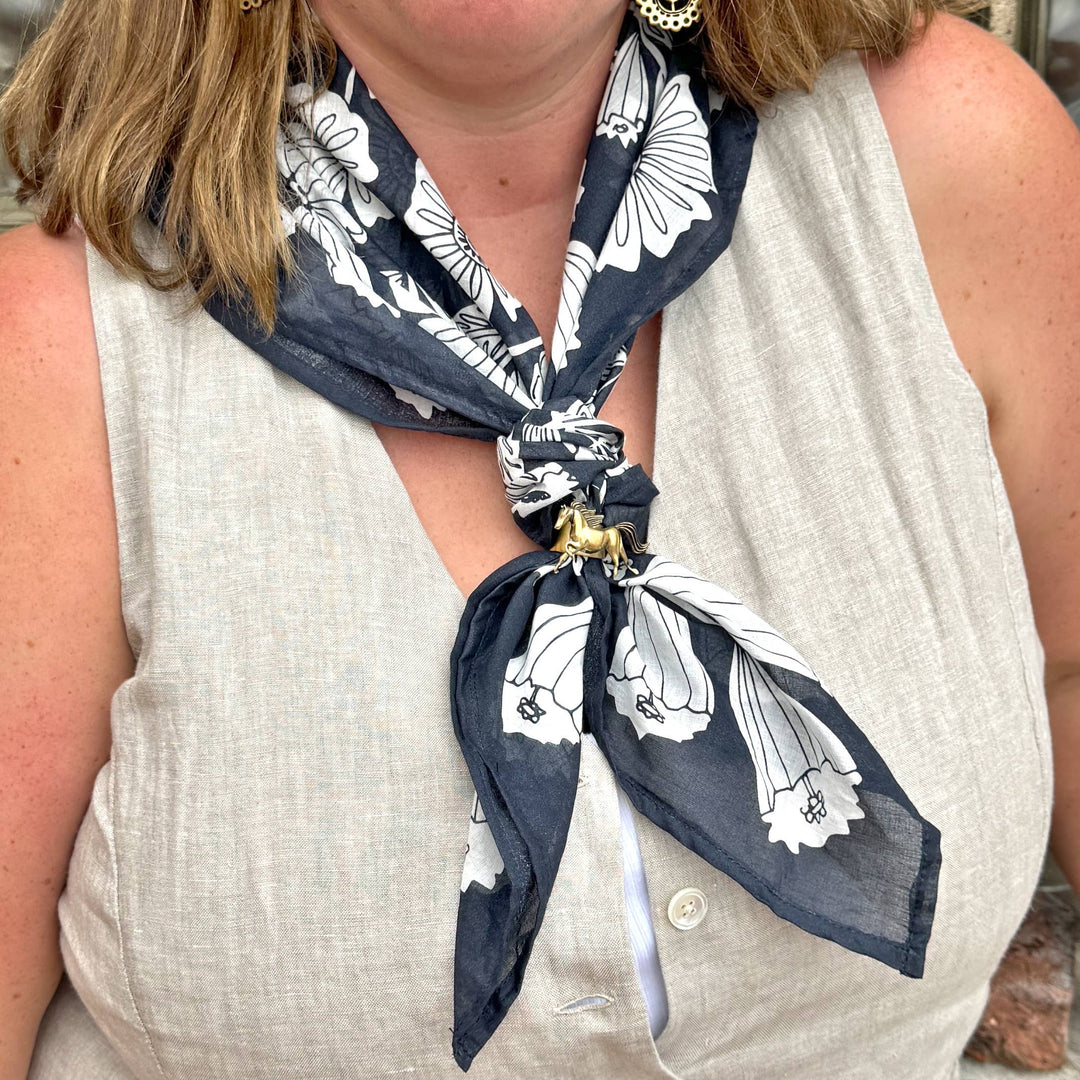 A person wears a sleeveless beige top with the Handker Bandanas 34" Wild Rag Fiona Bandana in dark blue and white, tied around their neck and secured with a gold scarf ring. Their face is partially out of view.