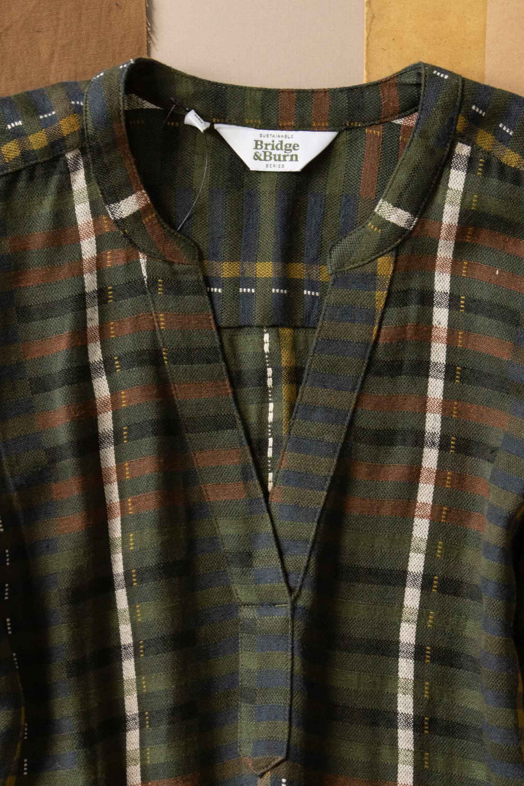 A close-up of the Bridge & Burn Ira Dress in Olive Stripe, featuring green plaid with brown, navy, and white stripes, a mandarin collar, partial button placket, and wrinkle-resistant fabric.