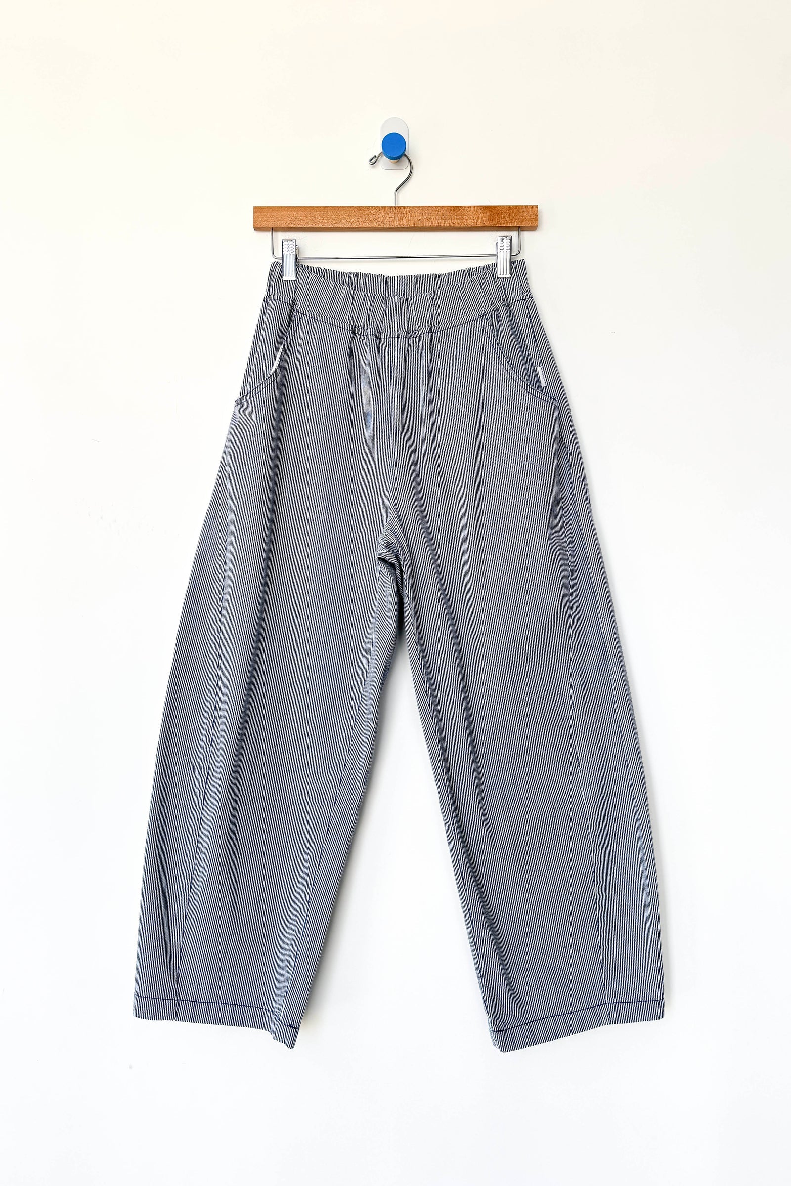 Le Bon Shoppe - Arc Pant in Blue Stripe features a wide-leg silhouette with an elastic waistband and convenient side pockets, crafted from heavyweight canvas for lasting durability. Displayed on a wooden hanger against a clean white background, these stylish everyday pants by Le Bon Shoppe are perfect for elevated comfort and style.