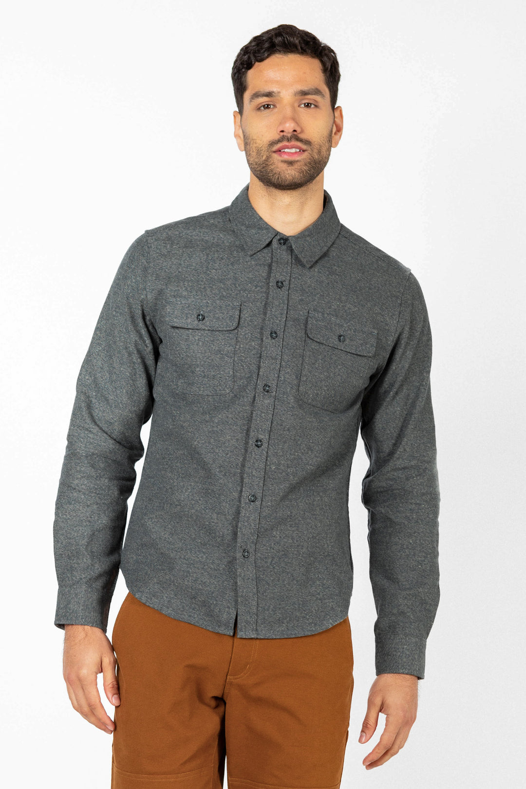 A man wearing the Bridge & Burn Cole Slim Shirt in Stone, featuring chest pockets, and brown pants stands against a plain white background.