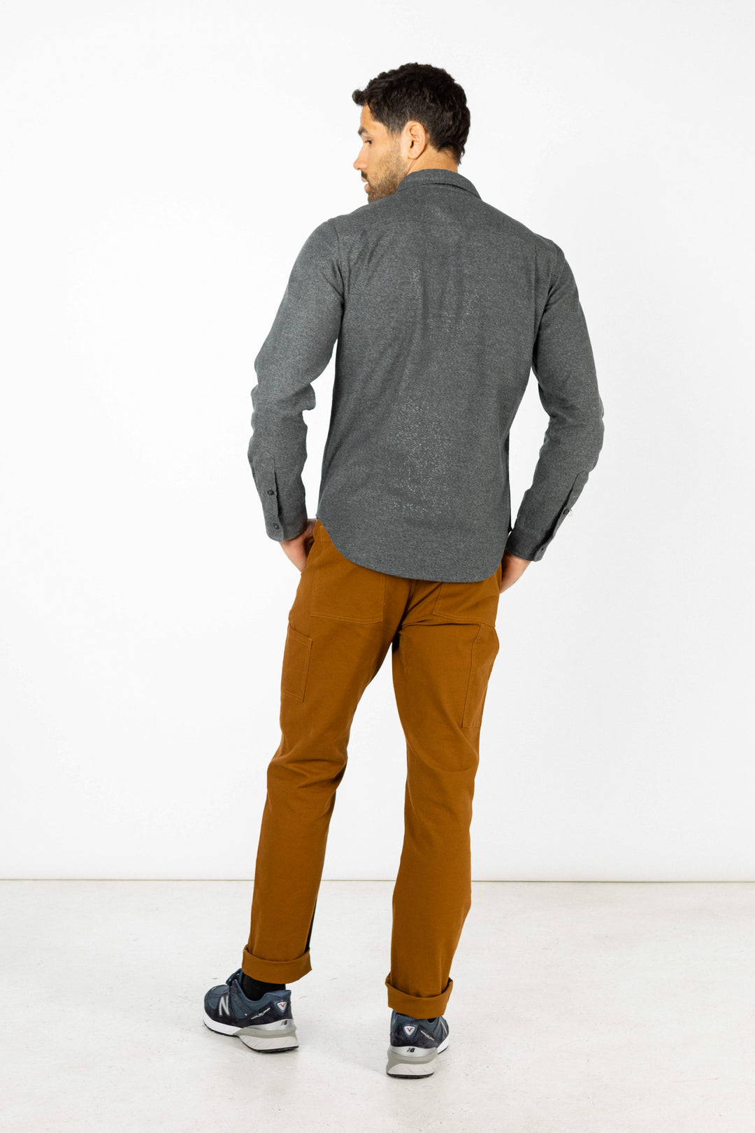 A man faces away from the camera, wearing the Bridge & Burn Cole Slim Shirt in Stone with brown pants and gray sneakers, standing against a plain white background.