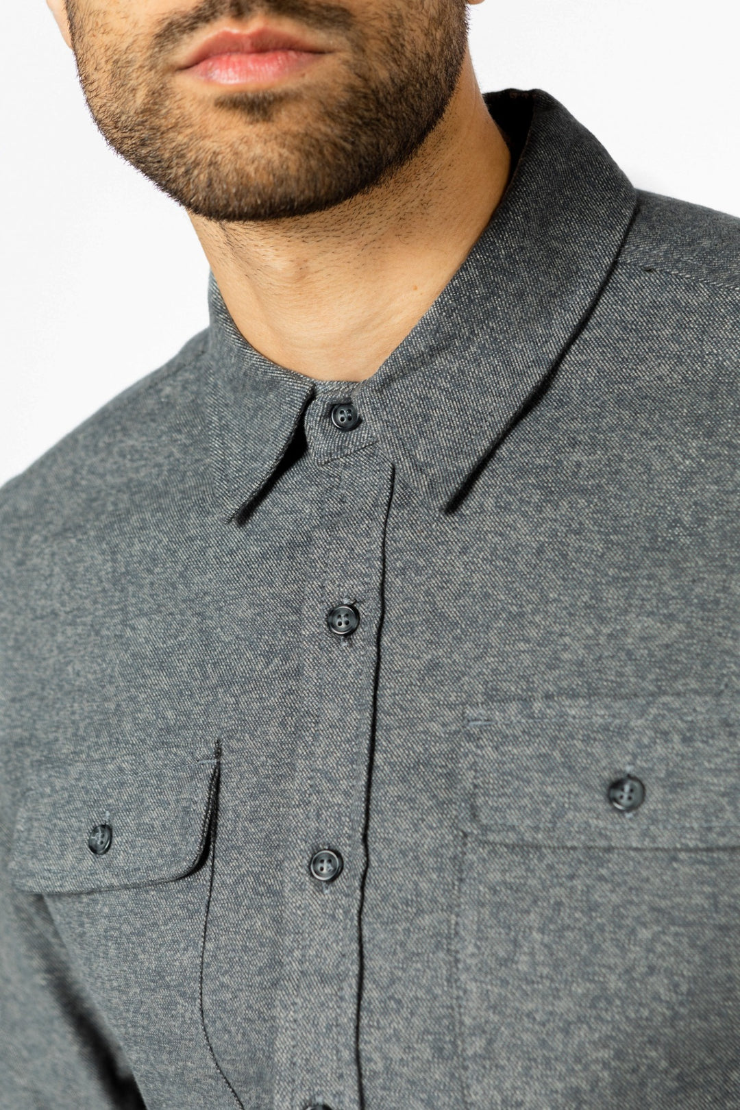 Close-up of a man wearing the Bridge & Burn Cole Slim Shirt in Stone, featuring a slim fit, two chest pockets, button-down collar, and visible buttons. The image shows his upper torso with part of his face and beard.