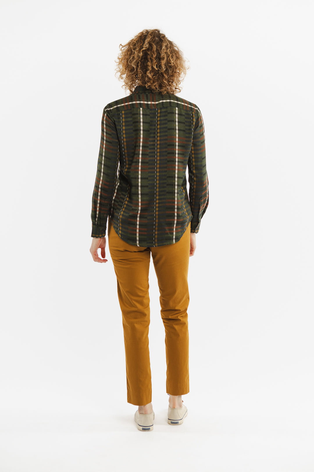 A woman wearing the Bridge & Burn Ash Slim Shirt in Olive Stripe stands before a white wall.
