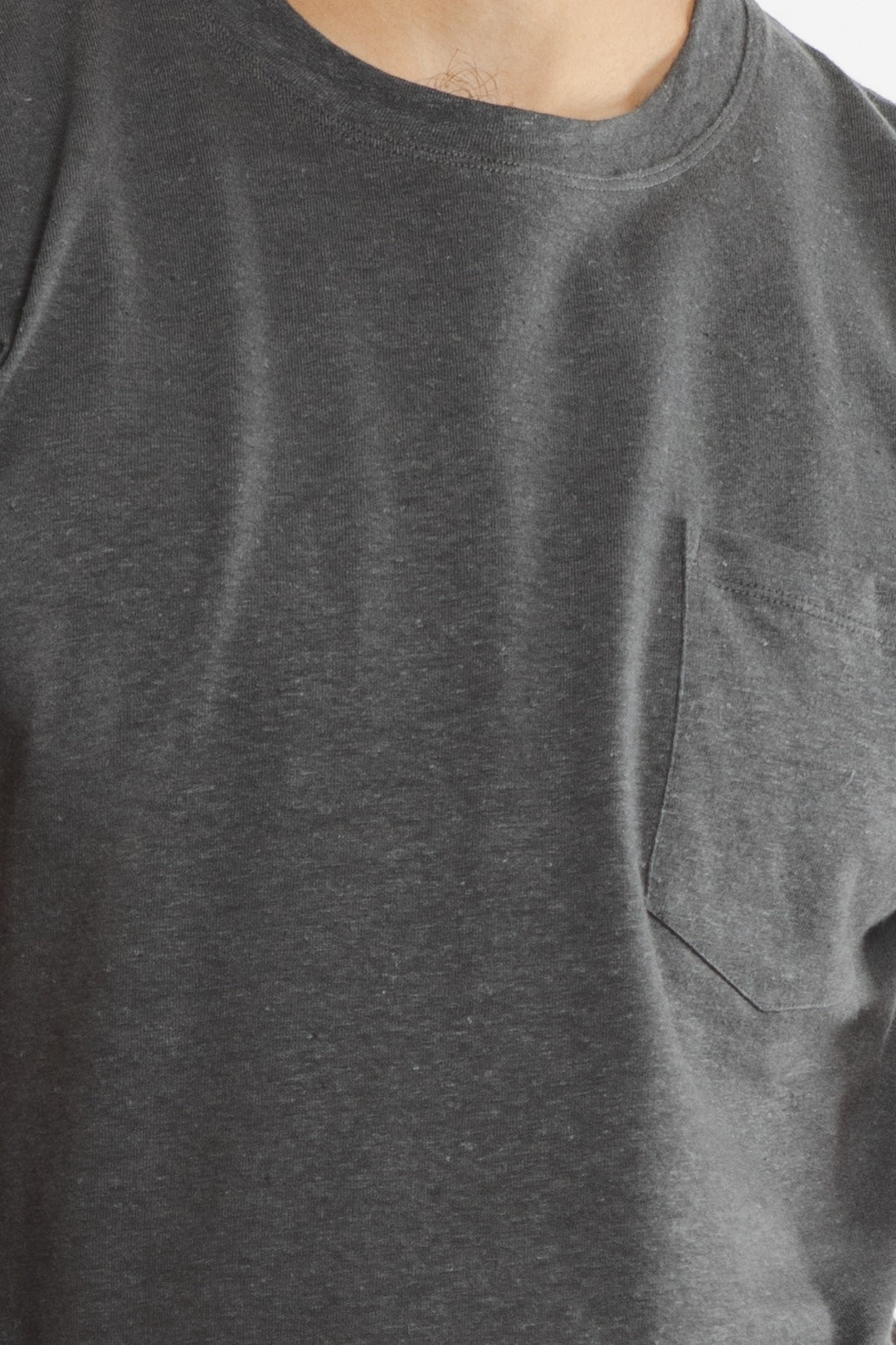 Close-up of a person wearing the Bridge & Burn Organic Hemp Pocket Tee in Slate Grey, featuring a chest pocket. Only the lower part of the neck and upper torso are visible.