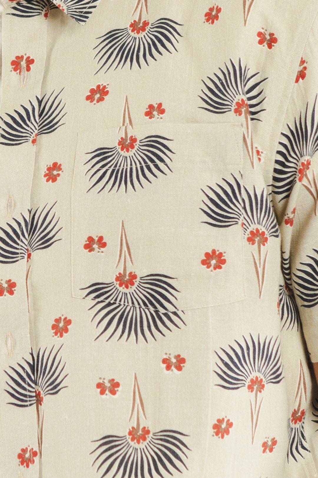 The Harbor Slim Shirt / Aloha Floral by Bridge & Burn is a beige slim fit shirt with a chest pocket, adorned with black palm-like leaves and small red floral designs. Made from a linen-cotton blend, it features visible buttons on the left side.