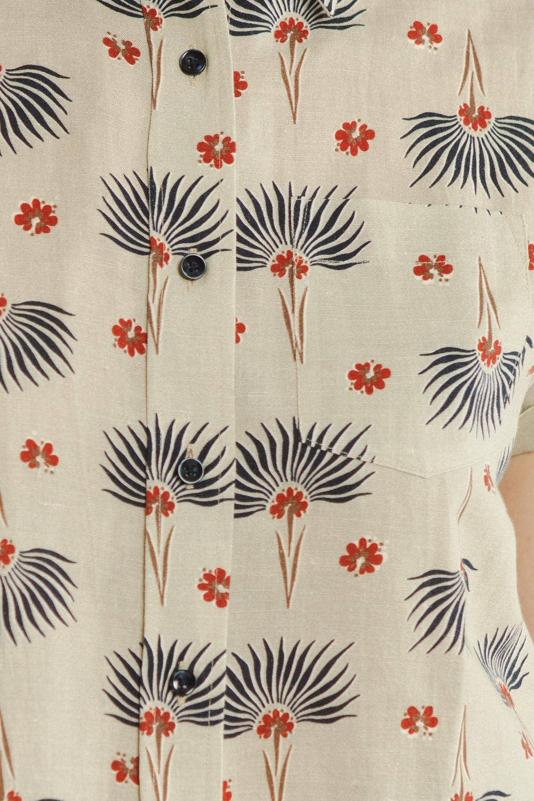 Close-up of the Bridge & Burn Bea Shirt / Aloha Floral: a beige short-sleeve button-down with black palm-like shapes, small red flowers, black buttons, and a visible right pocket.