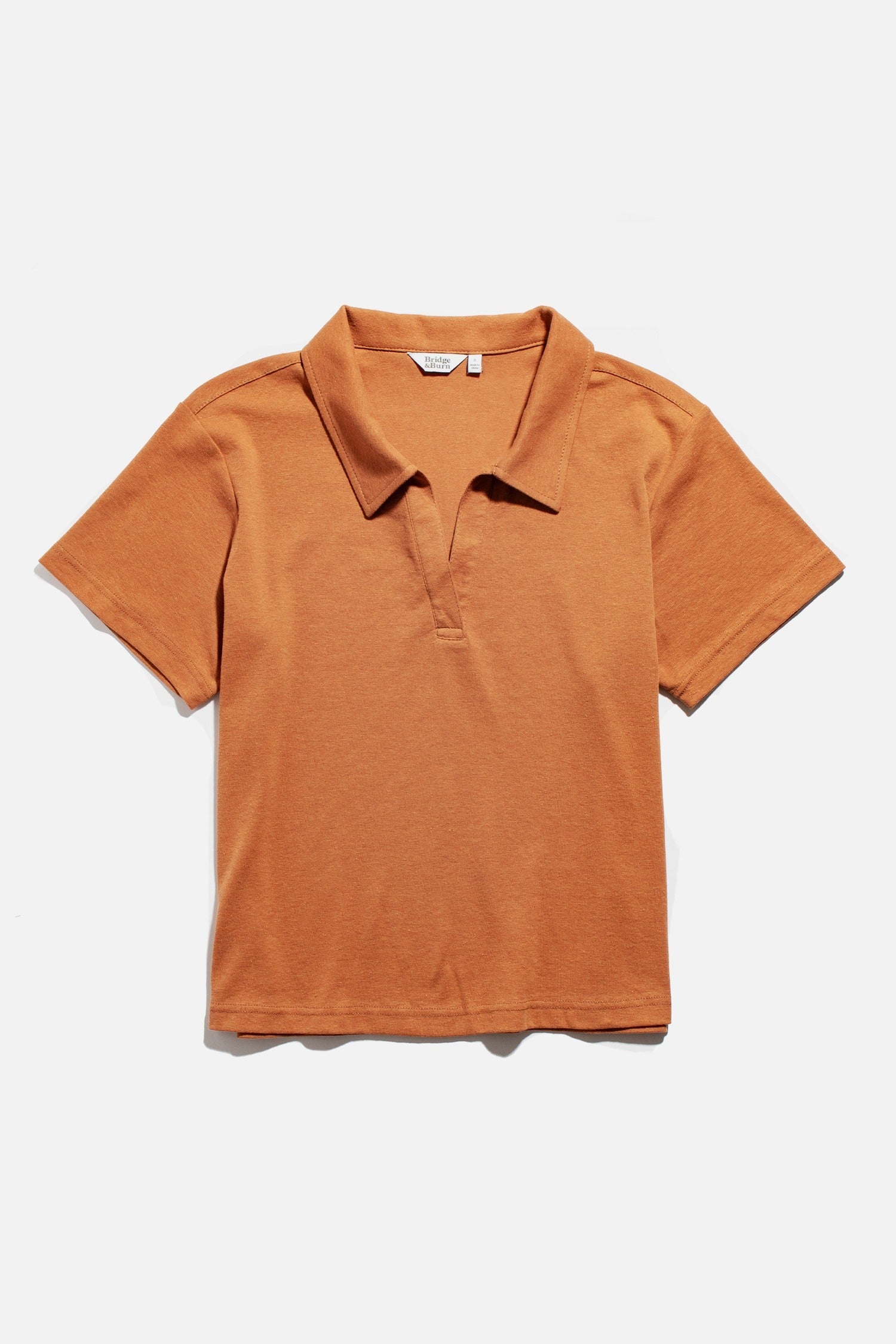 The Avery Boxy Top by Bridge & Burn is a short-sleeved, clay red jersey knit shirt with a collar and V-neck, shown laid flat on a white background.