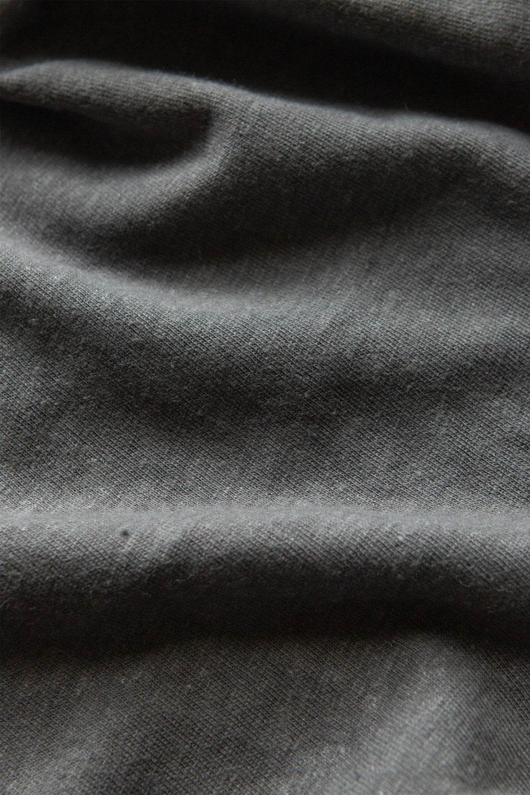 Close-up of the Organic Hemp Pocket Tee in Slate Grey by Bridge & Burn, highlighting its sustainable dark gray fabric with visible texture and soft, irregular folds and shadows.