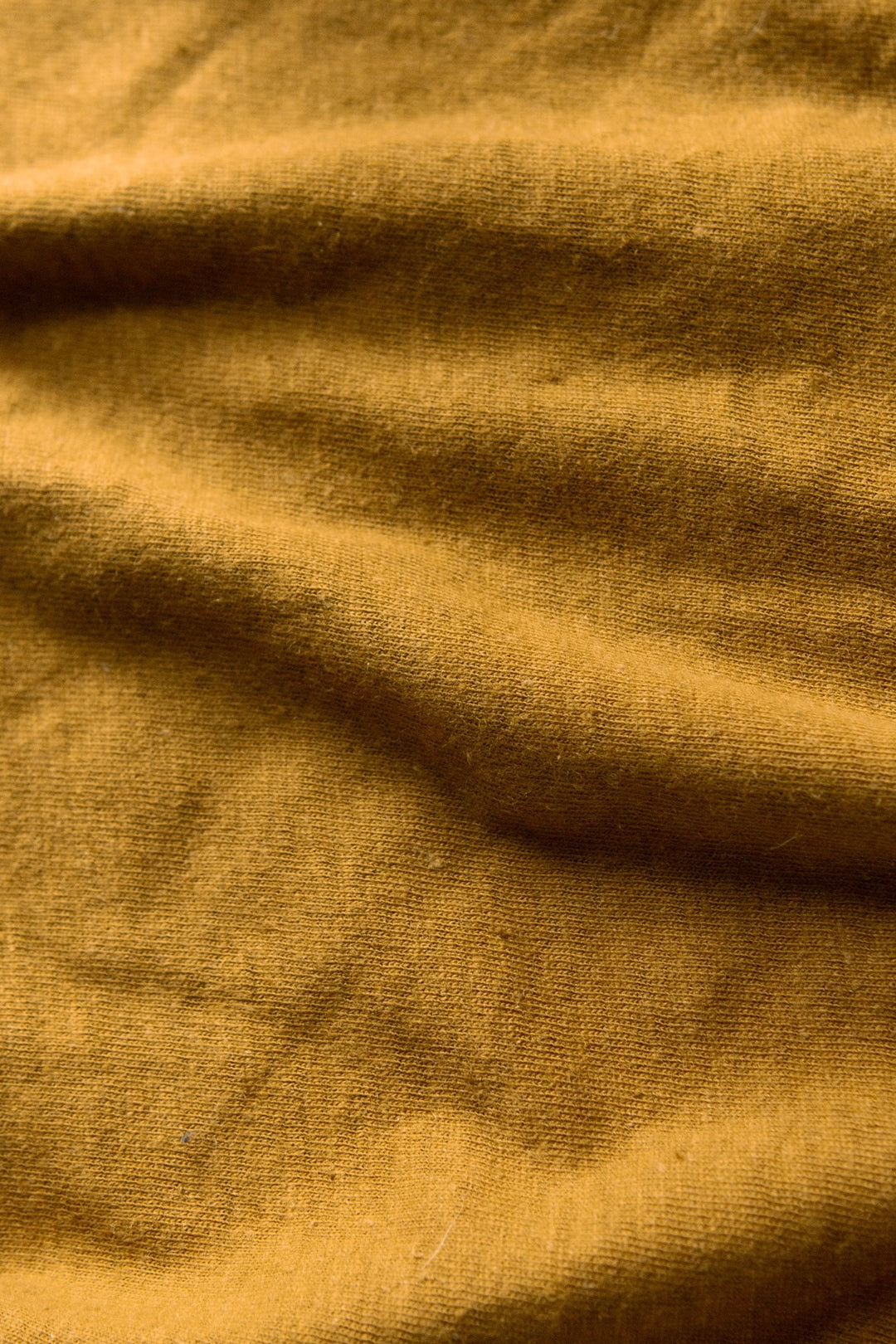 Close-up of Bridge & Burn's Organic Hemp Boxy Tee in Ochre, showing soft texture and natural folds. The fabric’s organic cotton-hemp blend appears slightly uneven, with gentle shadows and subtle color variations.