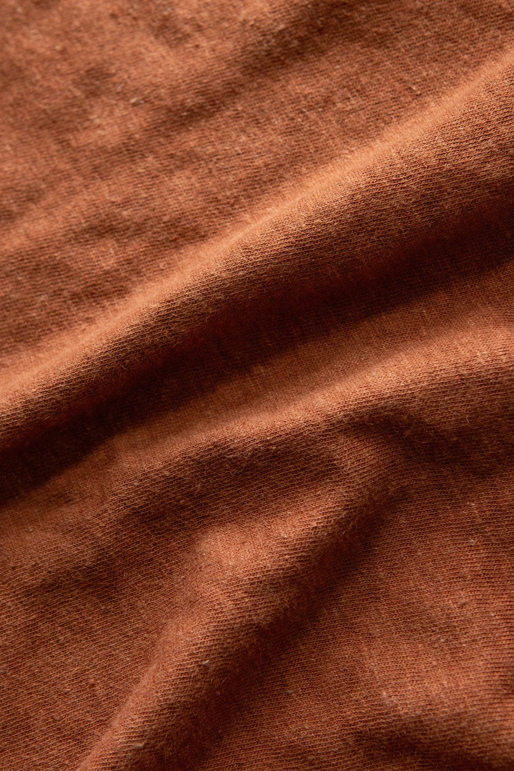 Close-up of the Organic Hemp Boxy Tee in Burnt Umber by Bridge & Burn, showing textured rust-colored fabric with soft folds and visible fibers for a cozy, vintage-inspired look.