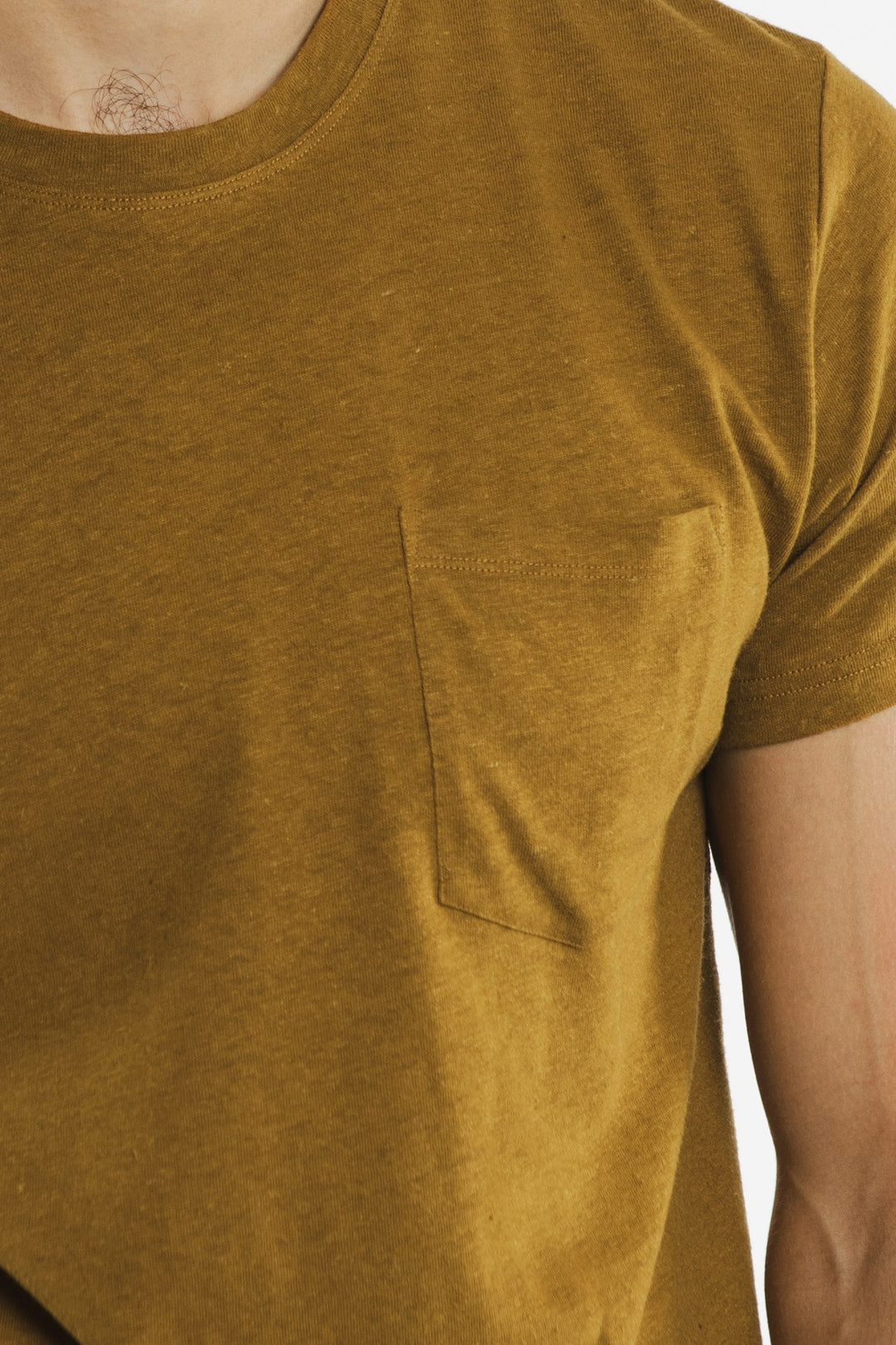A close-up of a person wearing the Bridge & Burn Organic Hemp Pocket Tee in Ochre, featuring a small chest pocket and showing the upper body, shoulder, and neck.