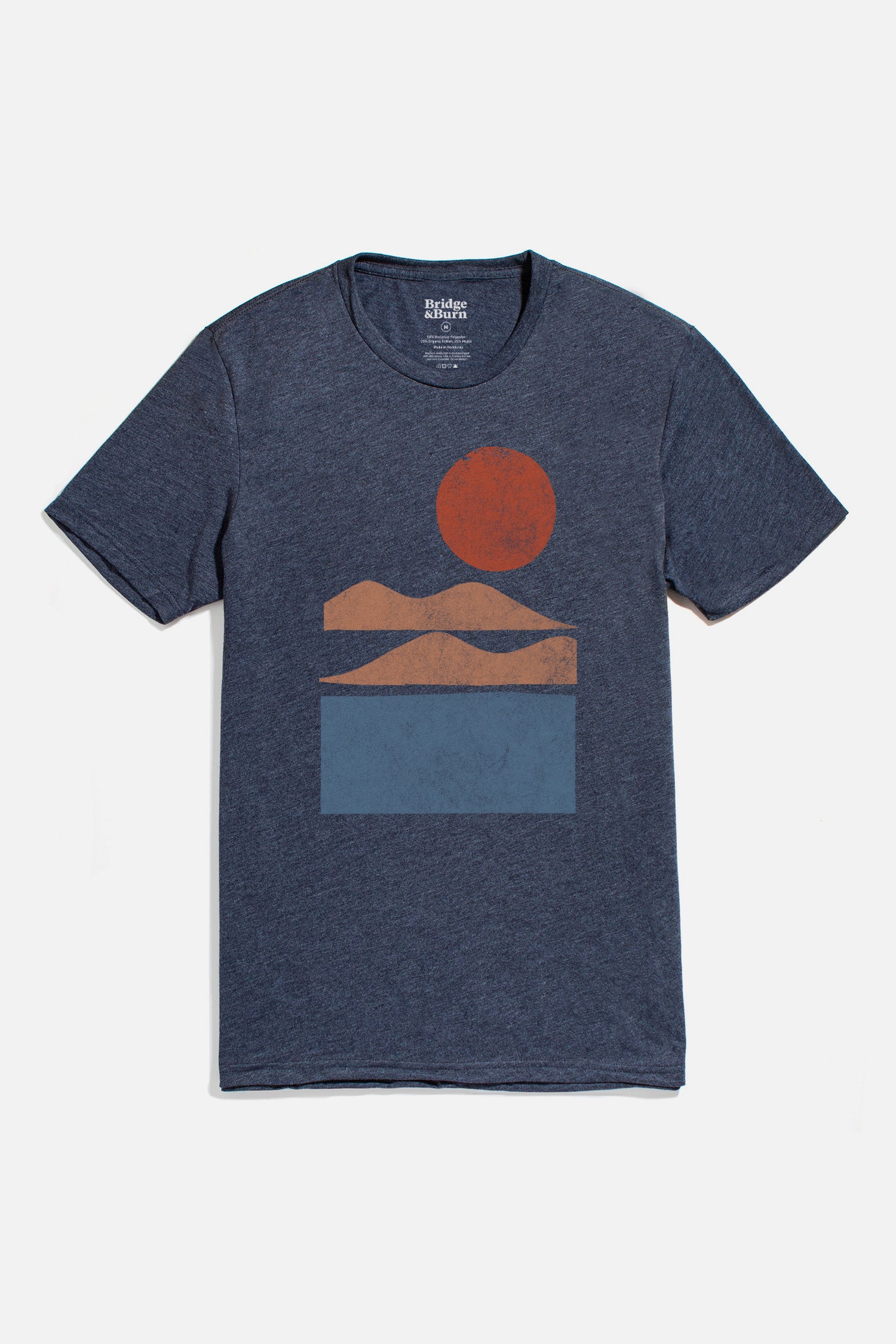 The Men's Alpenglow Tee in navy by Bridge & Burn is an eco-friendly shirt with a minimalist front design featuring orange mountains, a red sun, and a blue rectangle symbolizing water.