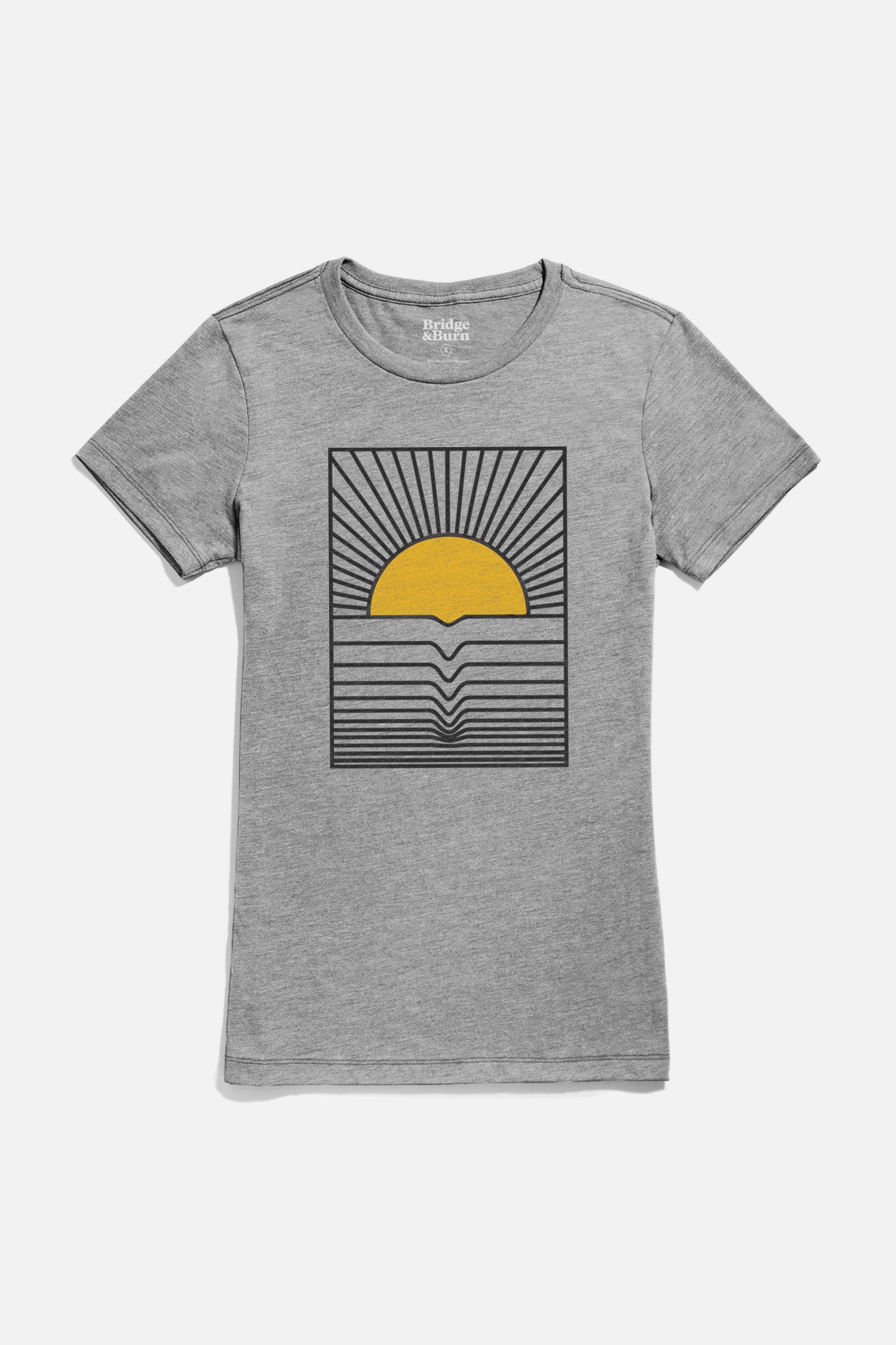 The Bridge & Burn Women's Cresting Wave Tee in grey is a lightweight shirt featuring a graphic of a yellow sun above the horizon, with black rays and wave-like lines suggesting water and reflection.