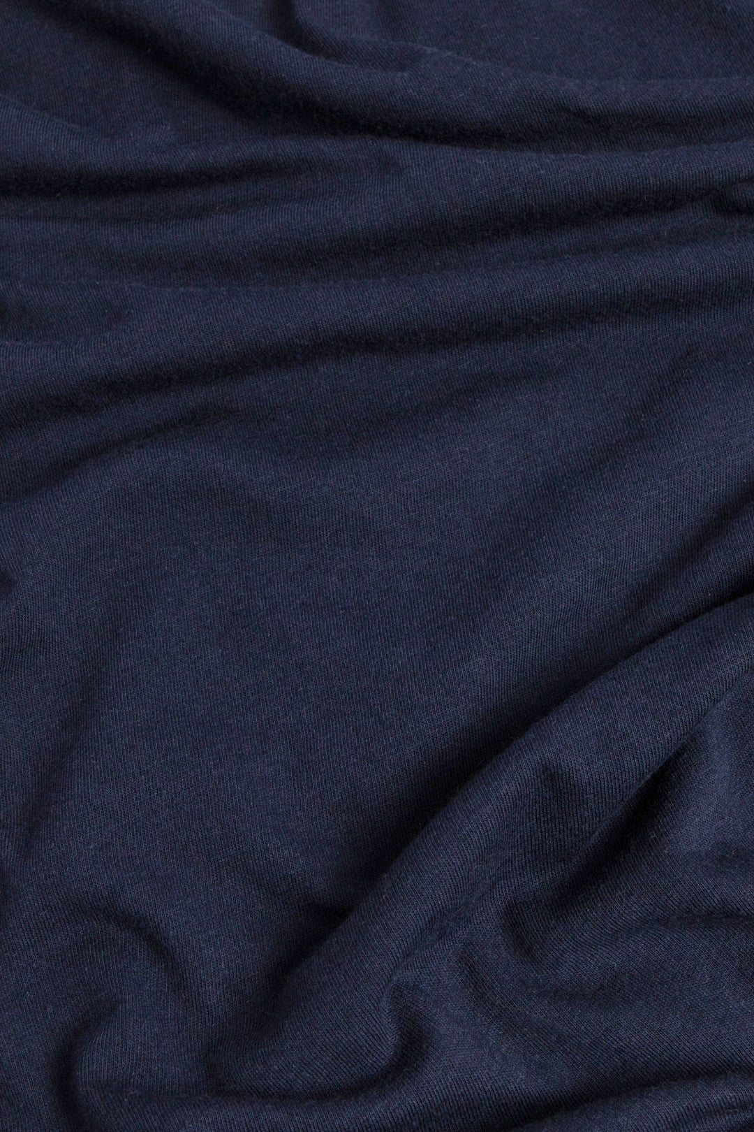 A close-up of the Women's Waves Tee in Navy by Bridge & Burn highlights the soft organic cotton fabric, featuring natural folds and wavy patterns across its surface.