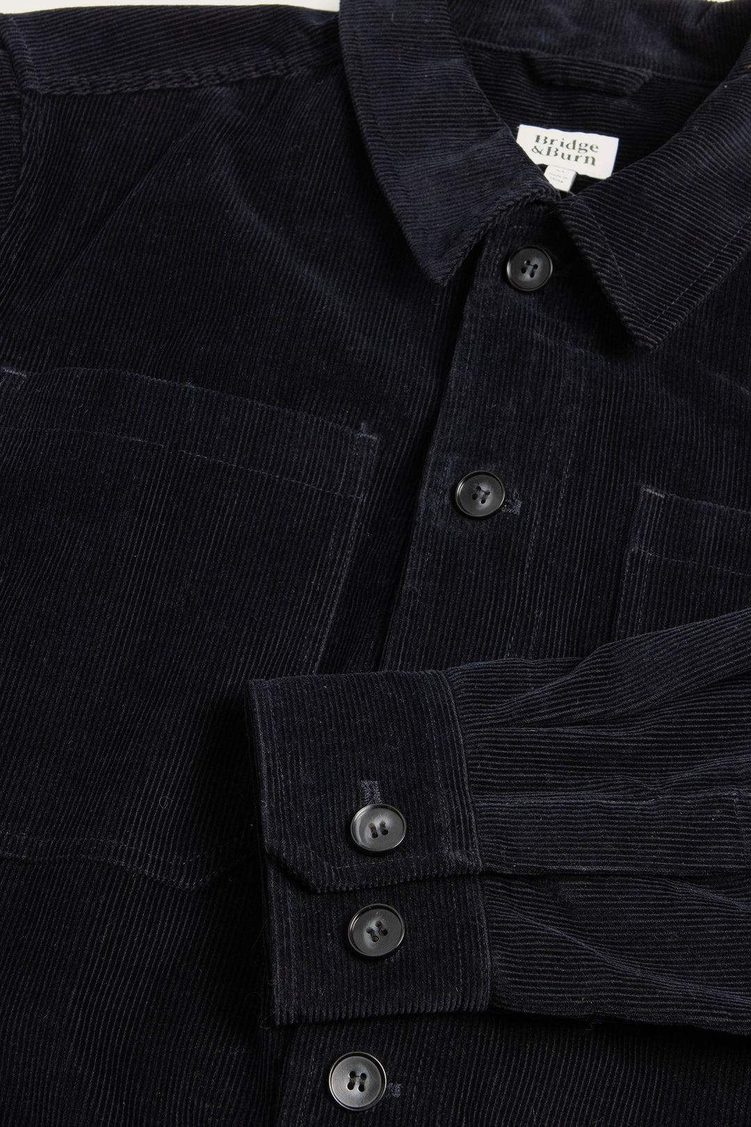 Close-up of the Banks Shirt Jacket by Bridge & Burn in Midnight Blue corduroy, featuring a collar, chest pocket, black buttons, and vertical ribbed texture—a soft yet sturdy workwear staple with a refined look.