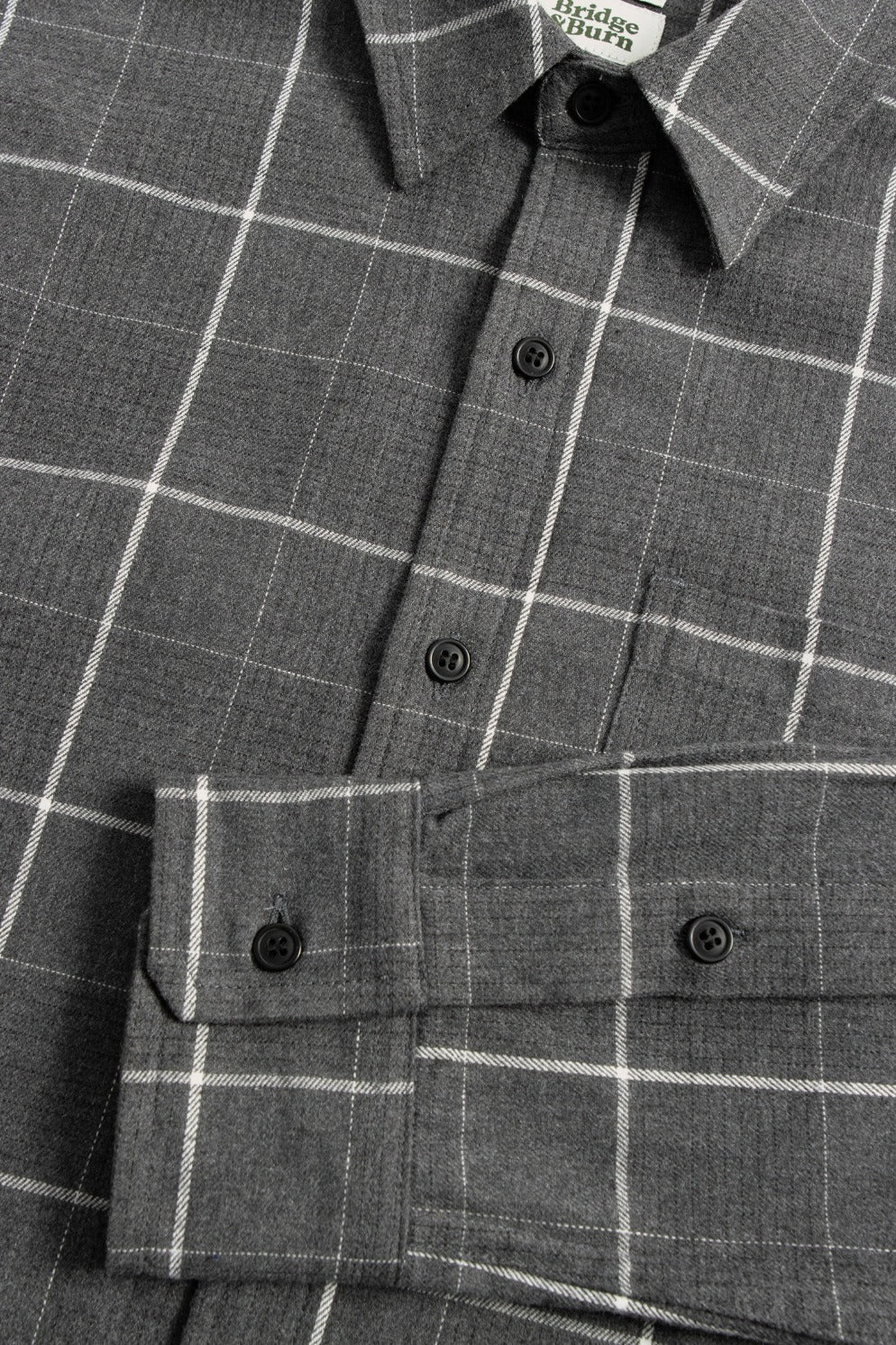 A close-up of the Bridge & Burn Larson Shirt in Shadow Twill Windowpane, featuring gray brushed flannel with a white check pattern, front buttons, collar, and part of the sleeve cuff.