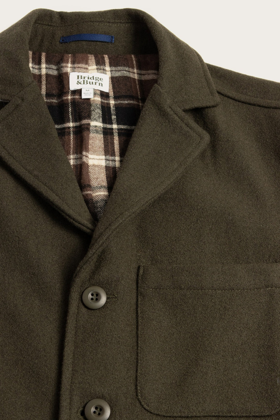 Close-up of the Nate Chore Blazer by Bridge & Burn in Basque Green wool, featuring a notched collar, brown buttons, chest pocket, and visible brown and cream plaid flannel lining.