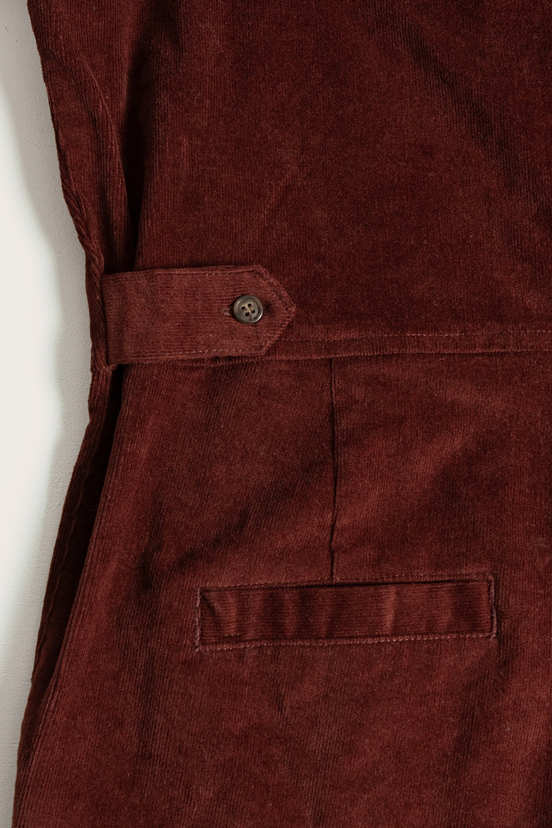 Close-up of the Faye Jumpsuit in Dark Red Pinwale by Bridge & Burn, featuring a side belt with button and welt pocket. The fine corduroy texture is clearly visible.