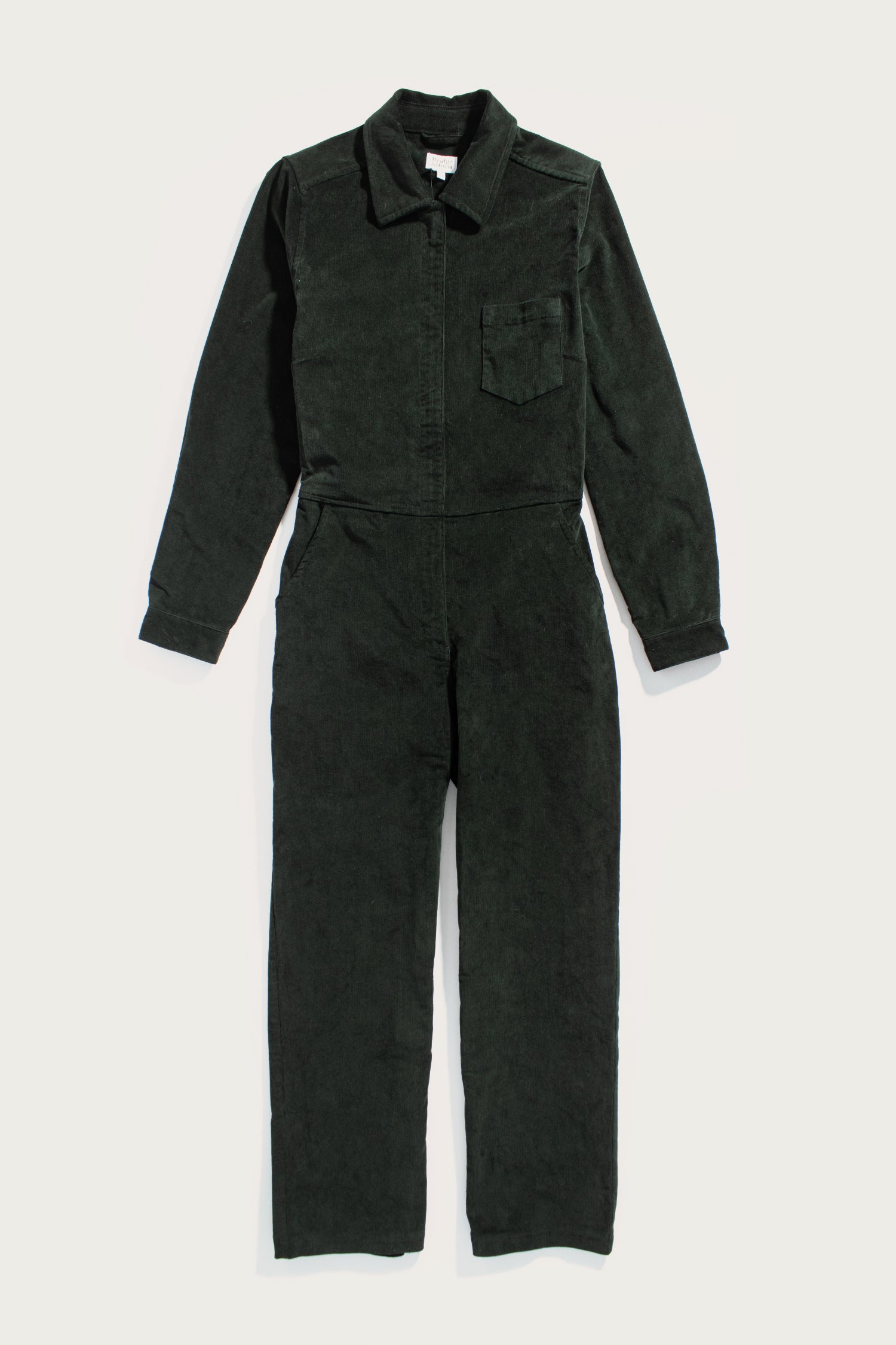 The Bridge & Burn Faye Jumpsuit in Deep Pine Pinwale is a pinwale corduroy workwear style with a collar, front zipper, chest pocket, and straight legs, laid flat on a white background.