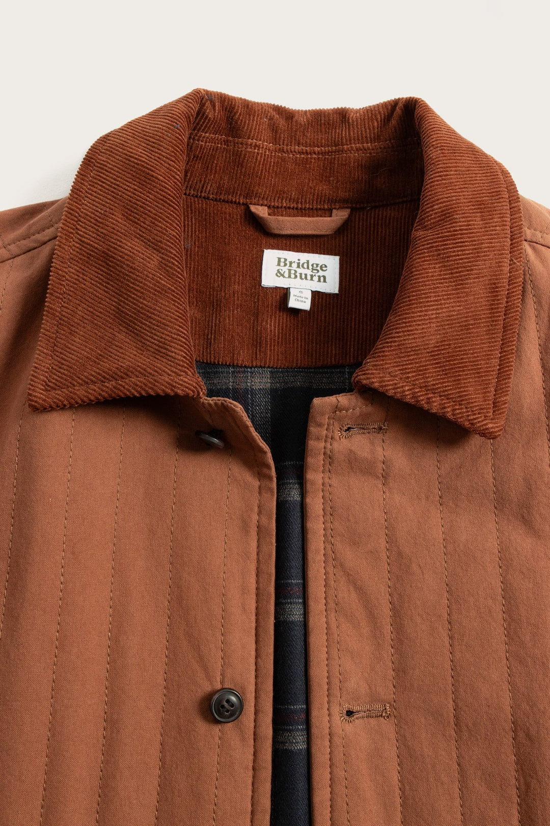 The Kenton Jacket in Sienna by Bridge & Burn features a rust hue, corduroy collar, vertical stitching, black buttons, and a plaid inner lining.