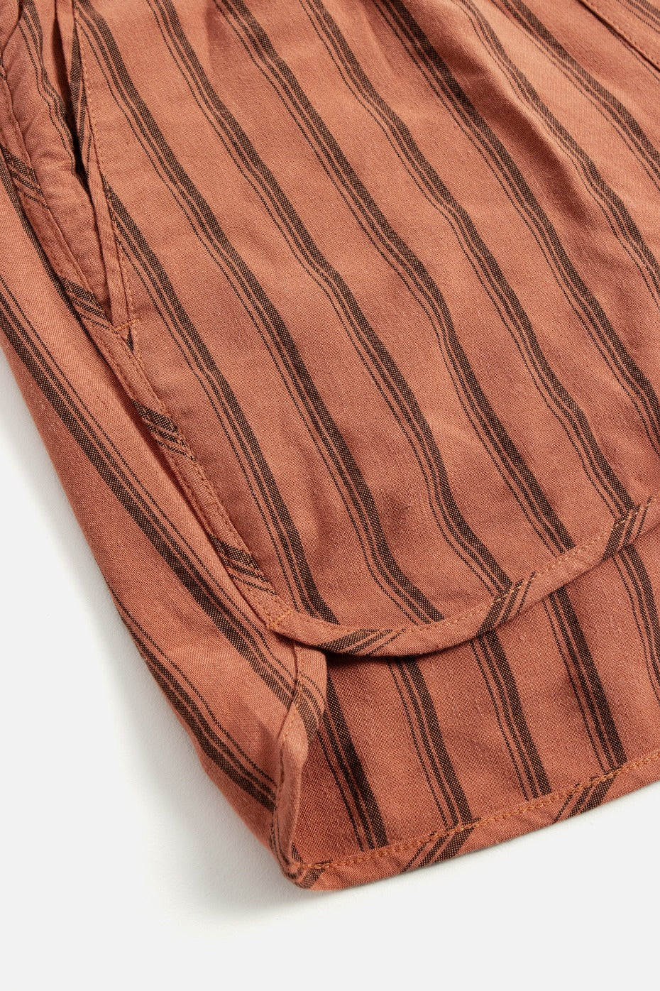 Close-up of Bridge & Burn's Luca Track Short in Rust Stripe, showing rust-colored fabric with vertical dark brown stripes and visible seams, laid flat on a white surface.
