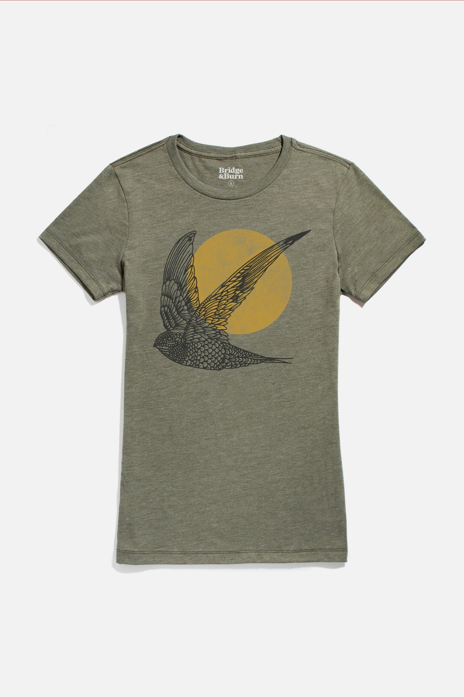 The Bridge & Burn Women's Flown Tee in olive is an organic cotton shirt with a black bird-in-flight design before a yellow-orange circle, crew neck, and short sleeves. Eco-friendly and stylish.