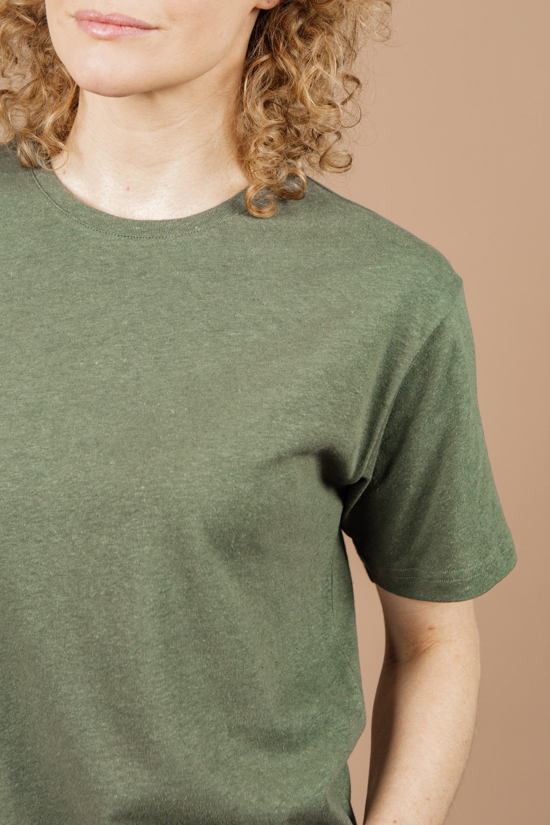 A person with curly blonde hair wears the Bridge & Burn Organic Hemp Boxy Tee in Cypress, shown from the shoulders up against a beige background.