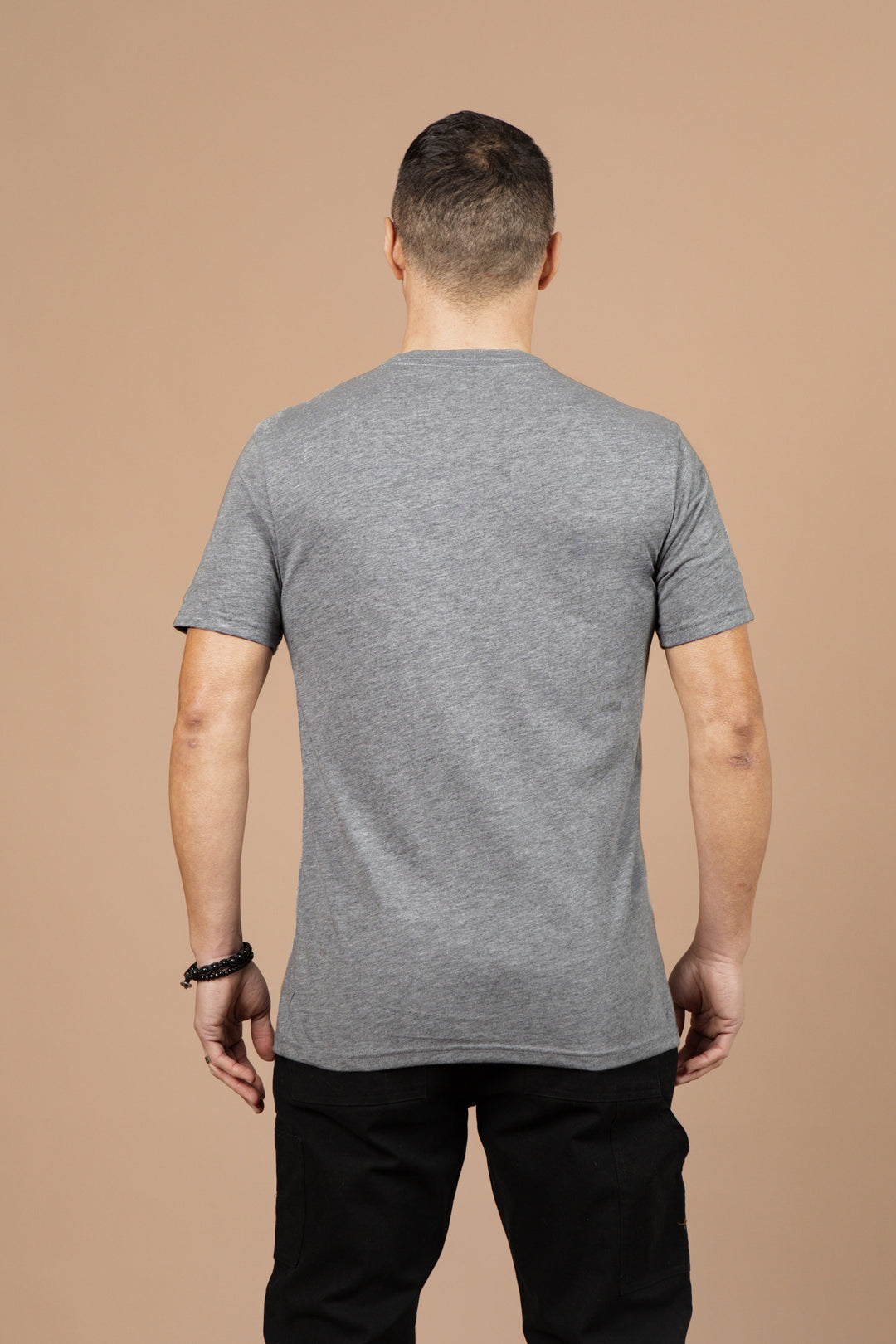 A man stands with his back to the camera, wearing the Bridge & Burn Men's Whiskey Will Do Tee in grey and black pants, set against a plain beige background.