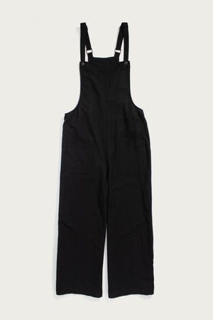 The Edie Overall in Black by Bridge & Burn is a wide-leg style with front pockets and adjustable straps, crafted from a soft tencel-cotton blend and shown laid flat on a white background.