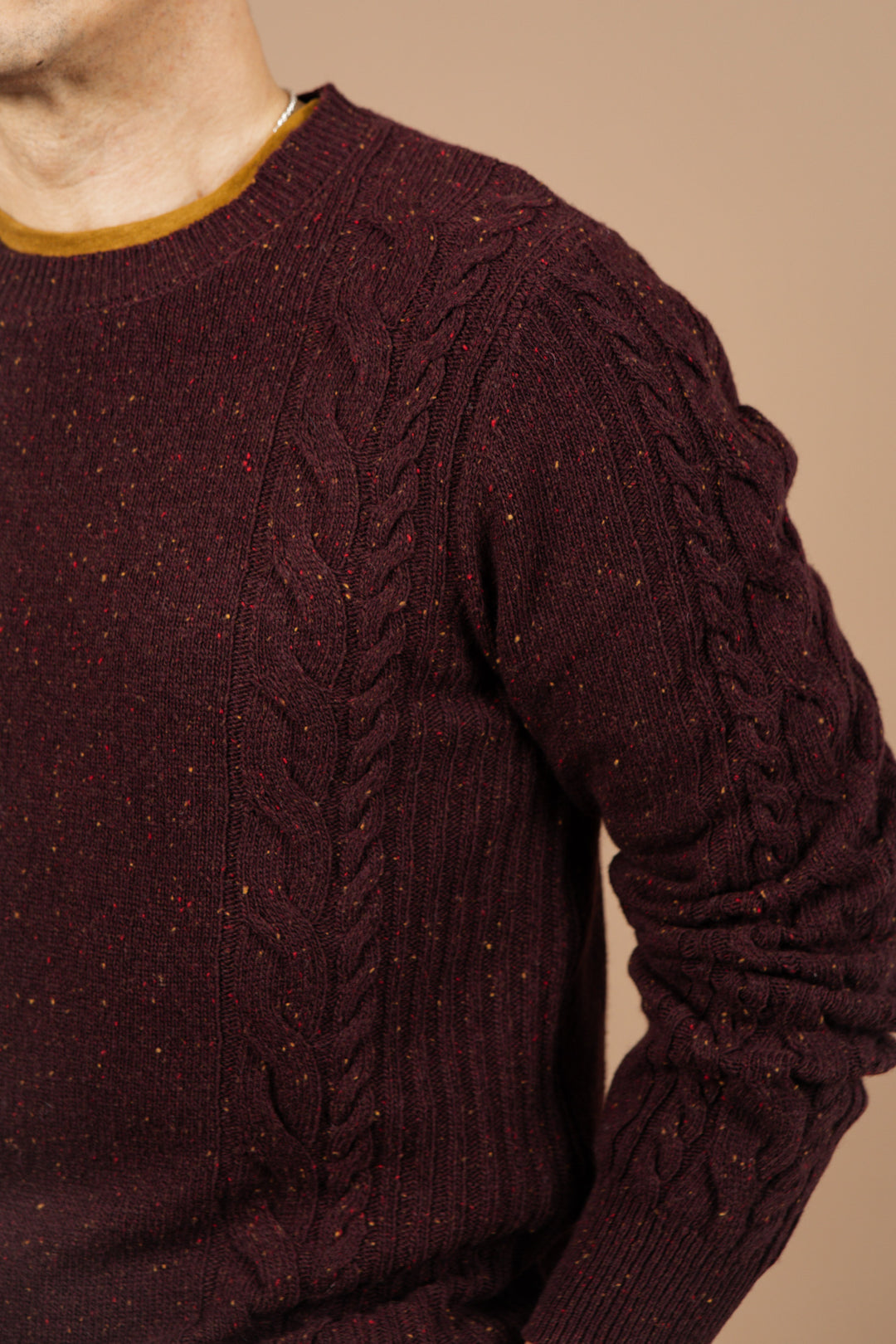 A person wears the Bridge & Burn Hugo Sweater in Burgundy Donegal over a brown shirt, shown from shoulders to waist against a beige background.