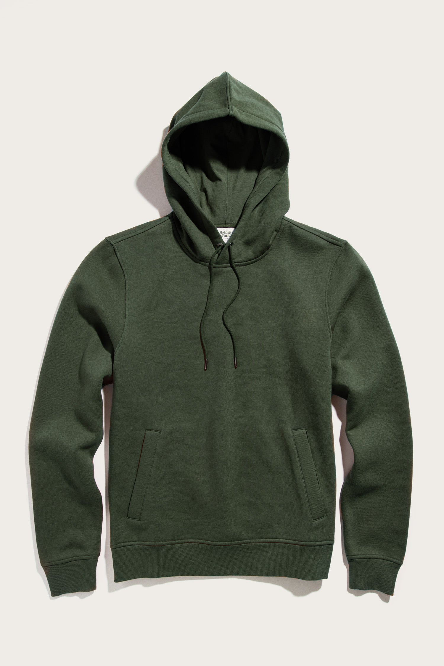The Williams Pullover Hoodie in Forest Night by Bridge & Burn, made from recycled polyester, features a drawstring hood and front pockets. Shown laid flat on a light background.