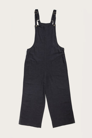 The Edie Overall in navy by Bridge & Burn is crafted from a soft linen-cotton blend, featuring adjustable shoulder straps and two large front pockets, displayed flat on a white background.