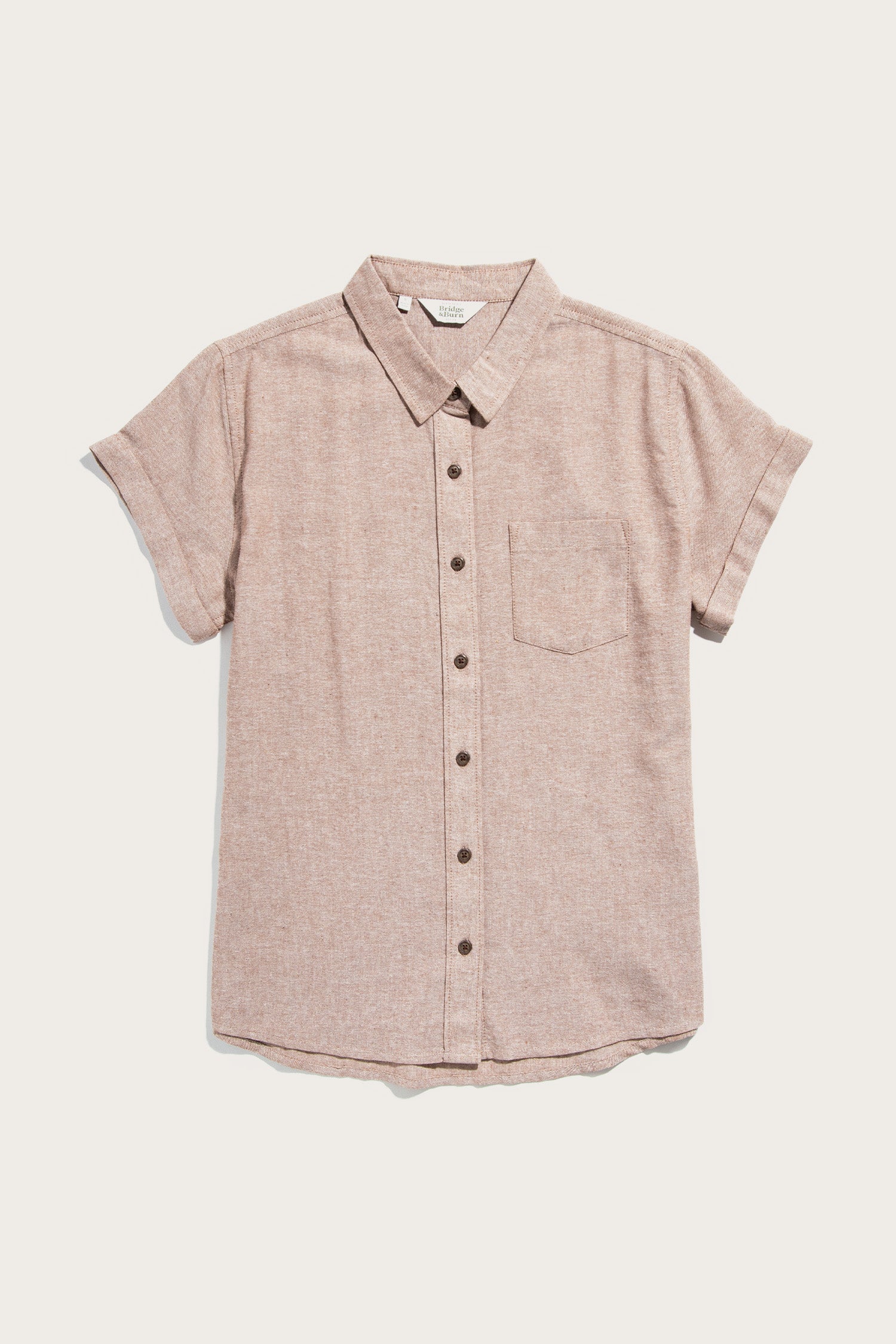 The Bridge & Burn Bea Shirt in Rust Chambray is a short-sleeve, light brown button-down made from recycled cotton with a single chest pocket, spread collar, and rolled cuffs, shown laid flat on a white background.