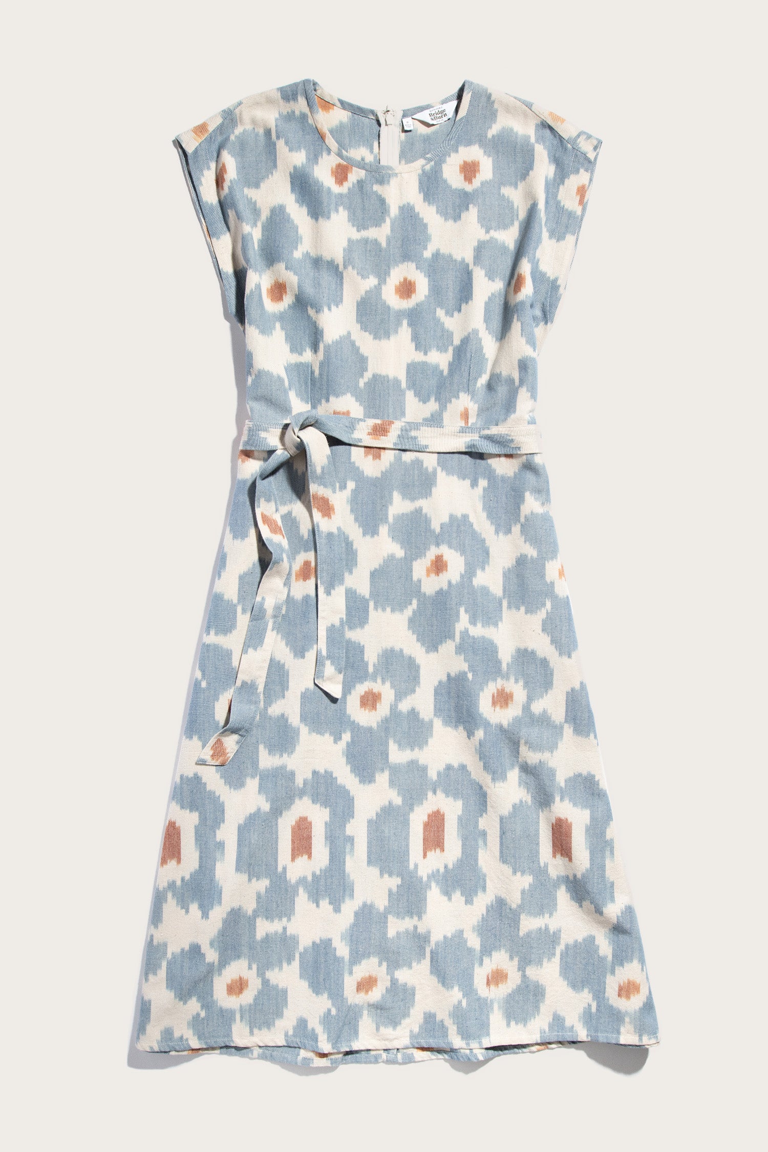 The Eloise Dress / Polar Blossom by Bridge & Burn is a short-sleeve, knee-length A-line dress featuring a blue and white abstract print with orange accents, a round neckline, matching fabric belt, and is shown laid flat on white.