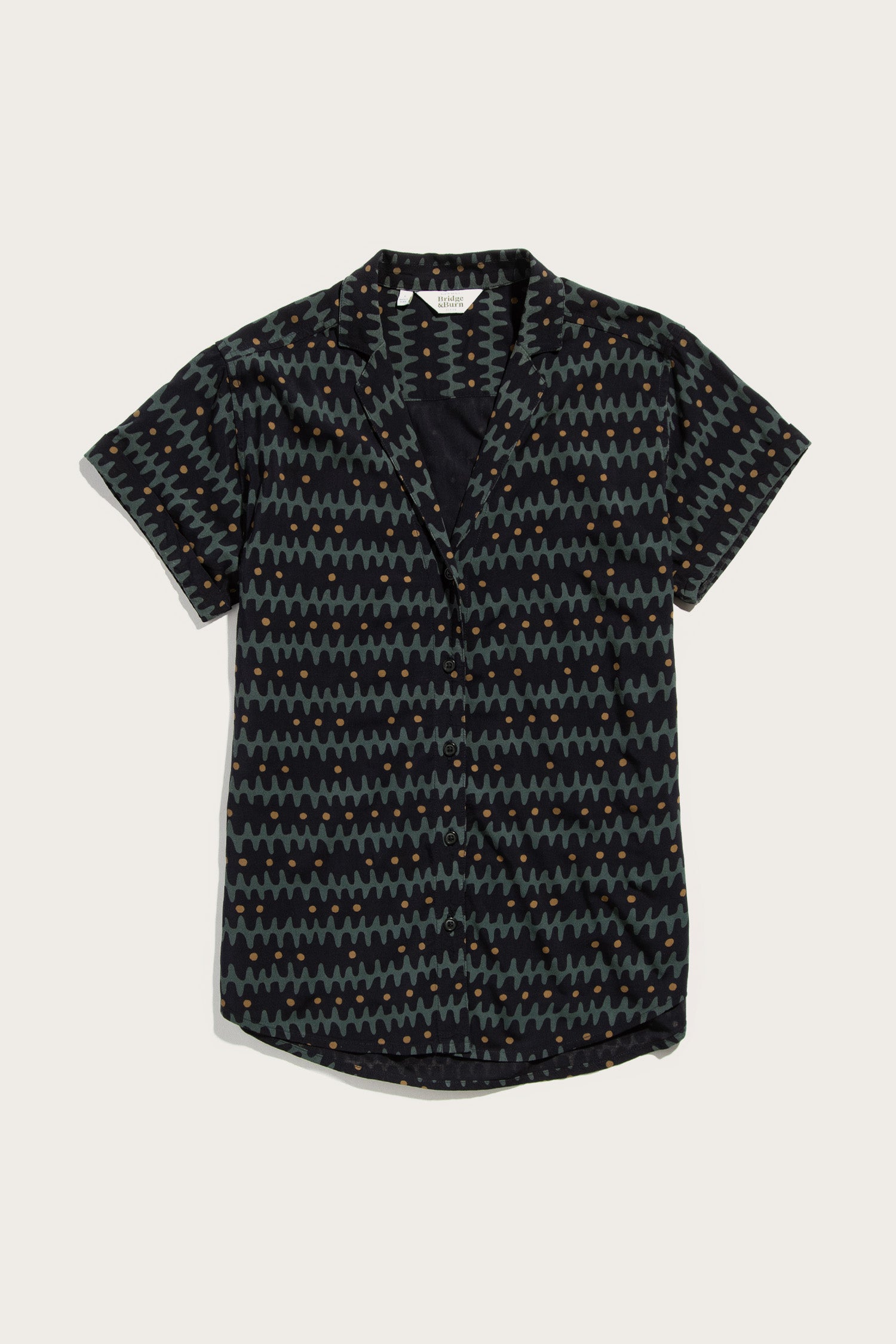 The Bridge & Burn Innes Shirt in Fishbone Ink is a relaxed-fit, short-sleeve button-up featuring a dark base with blue, green, and orange geometric zigzags and dots, finished with a modern lapel collar.