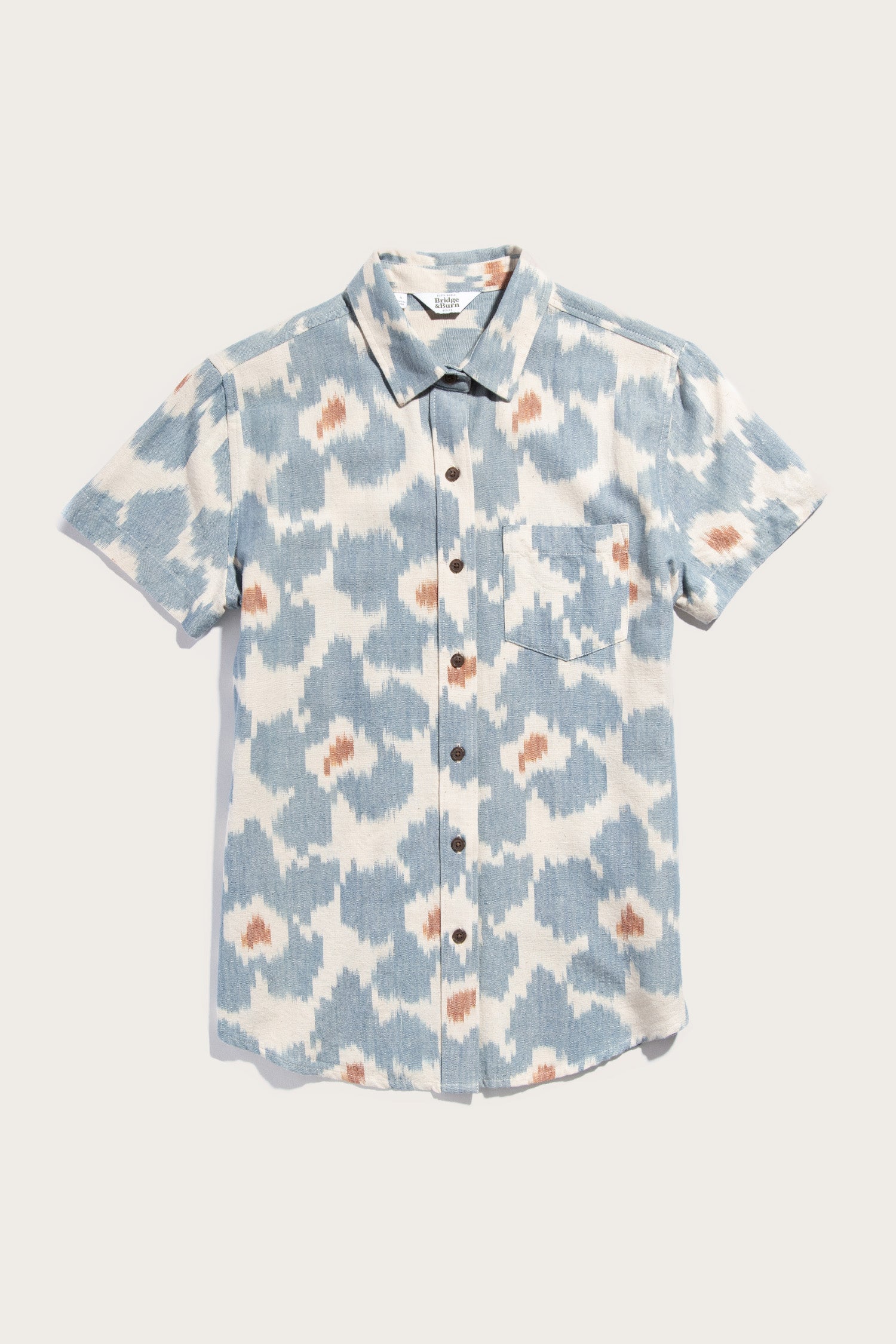 The Bridge & Burn Lana Shirt in Polar Blossom is a relaxed fit, short sleeve button up with a blue, white, and brown abstract print. Made from 100% cotton, it features a classic collar and single chest pocket. Shown against a white background.