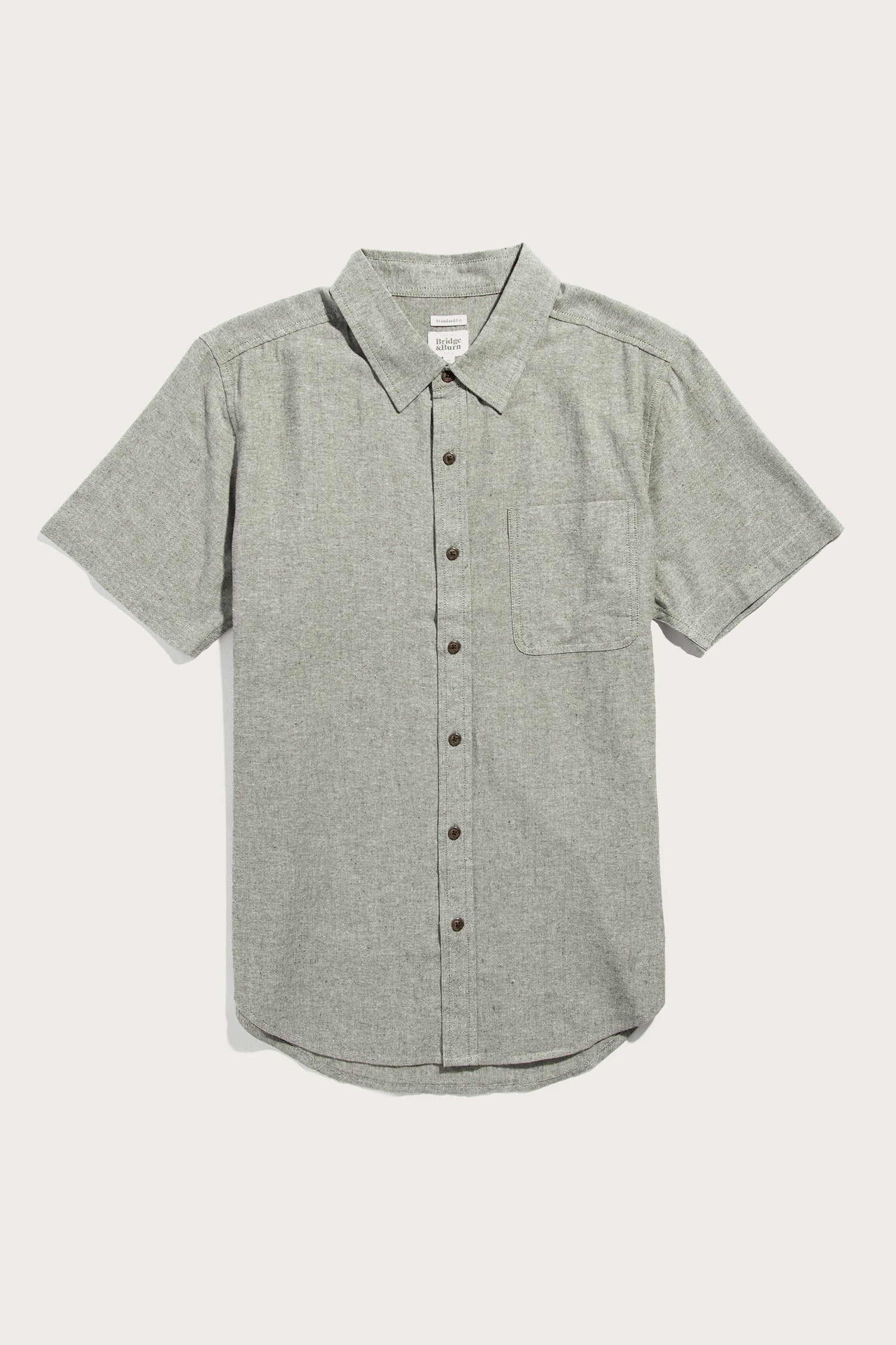 The Bridge & Burn Malcolm Shirt in Sage Chambray is a sustainable men's short-sleeve button-up with a collar and single chest pocket, shown in light gray on a plain white background.