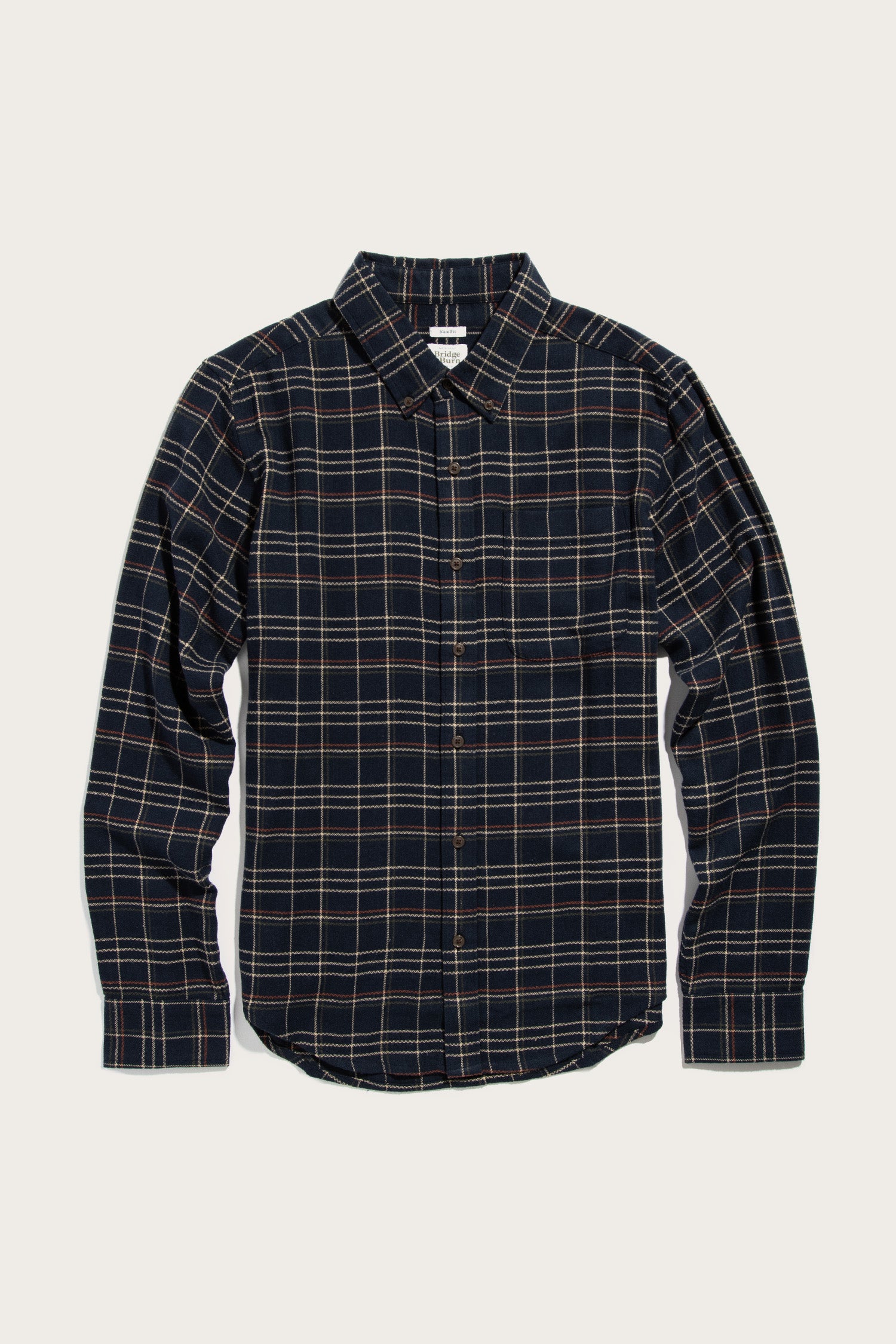 Bridge & Burn's Sutton Slim Shirt in Dusk Herringbone Plaid is a slim-fit, long-sleeve button-up with a navy and beige plaid pattern, classic collar, and single chest pocket, shown laid flat on a light background.